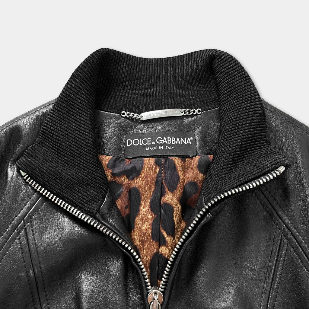 A close-up view of a black leather jacket with a collar and zipper, featuring a leopard print pattern inside the lining.