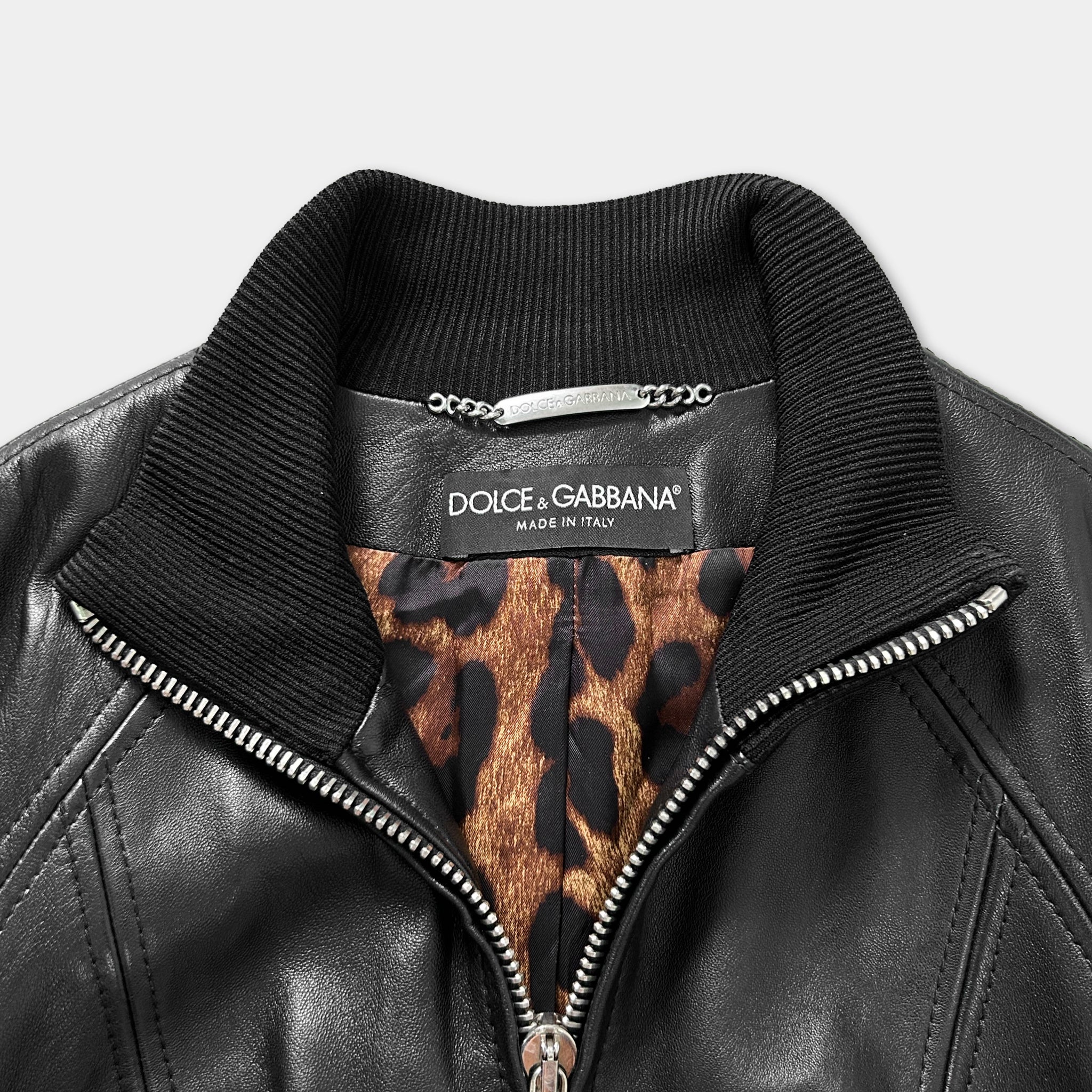 A close-up view of a black leather jacket with a collar and zipper, featuring a leopard print pattern inside the lining.