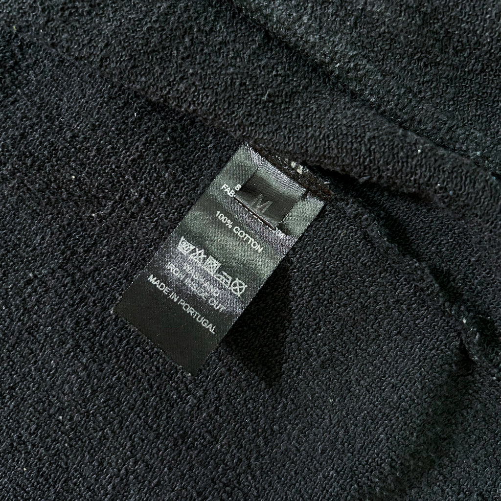 a close-up view of a black fabric, possibly a sweater or garment, with a black label attached to it. The label appears to be a care label or instructions label, providing information about the fabric and care instructions for the garment.