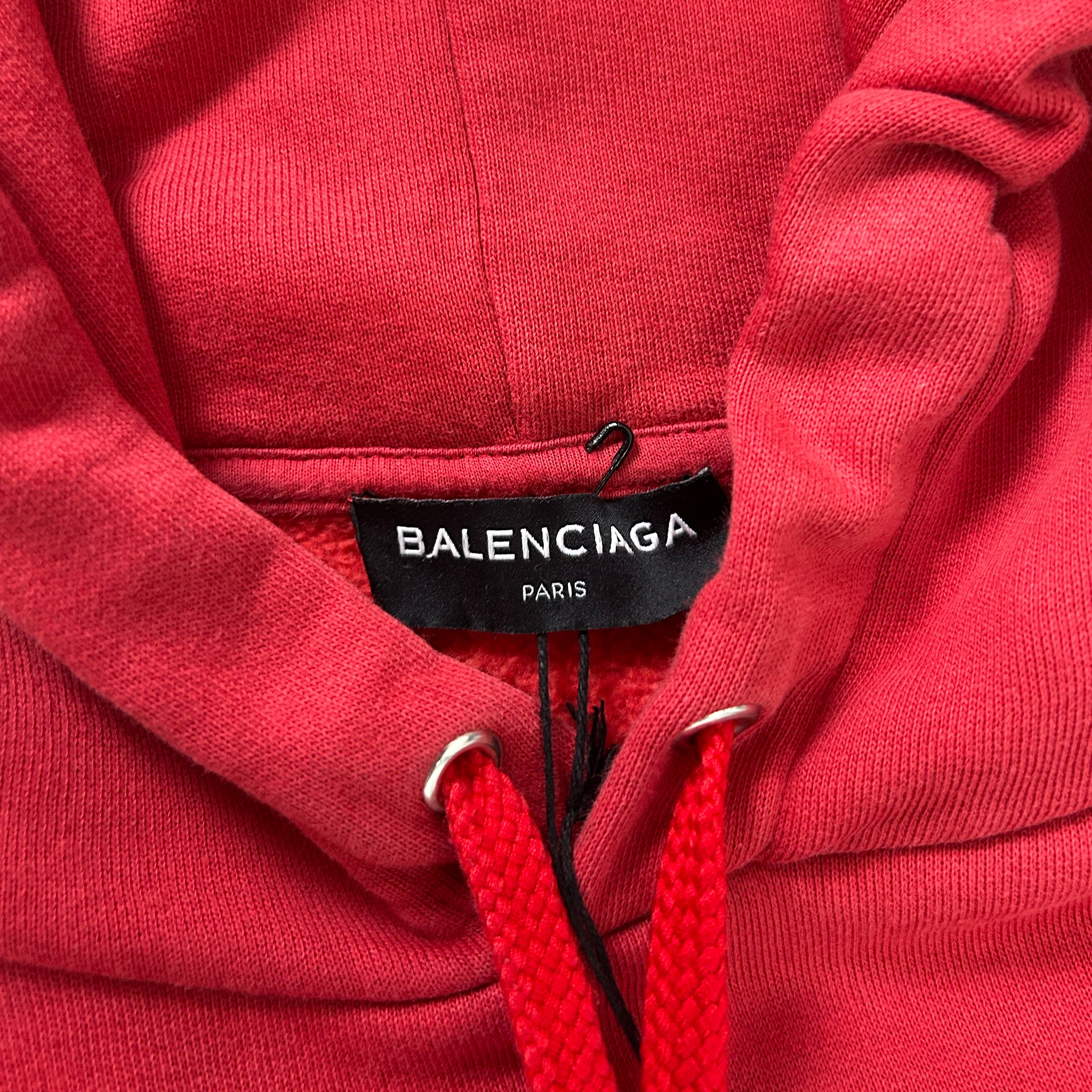 A close-up view of a red Balenciaga hoodie, showing the brand name and tag on the fabric.
