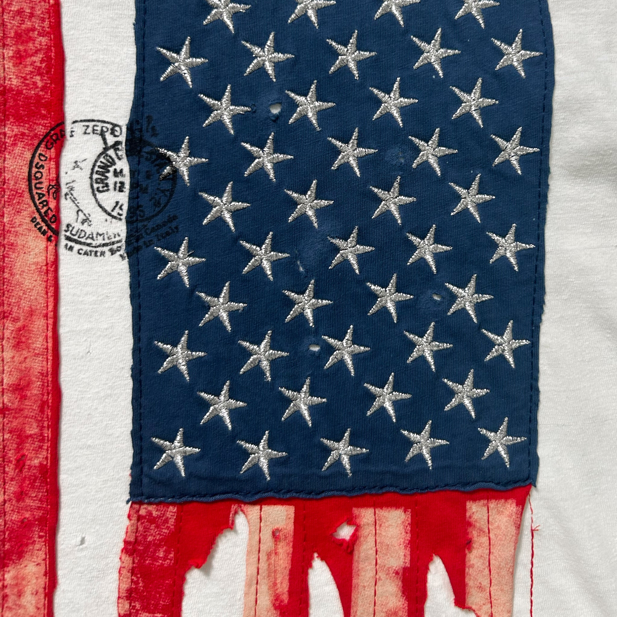 The image is a close-up of a fabric with a pattern of stars, resembling the American flag. The fabric appears to be torn or damaged, with frayed edges and a faded appearance.