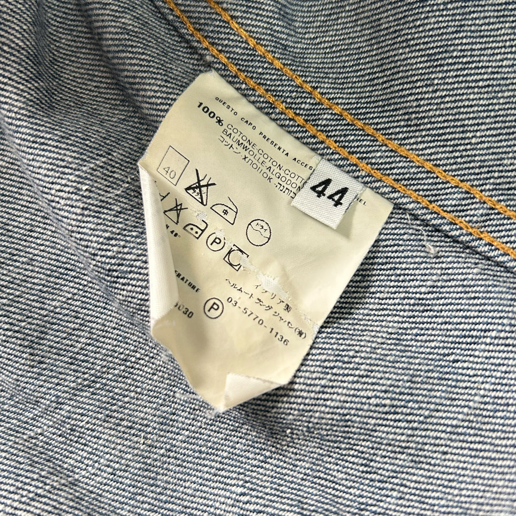 a close-up view of a denim fabric, with a label attached to it. The label appears to be a care label, providing instructions for washing and drying the denim fabric.