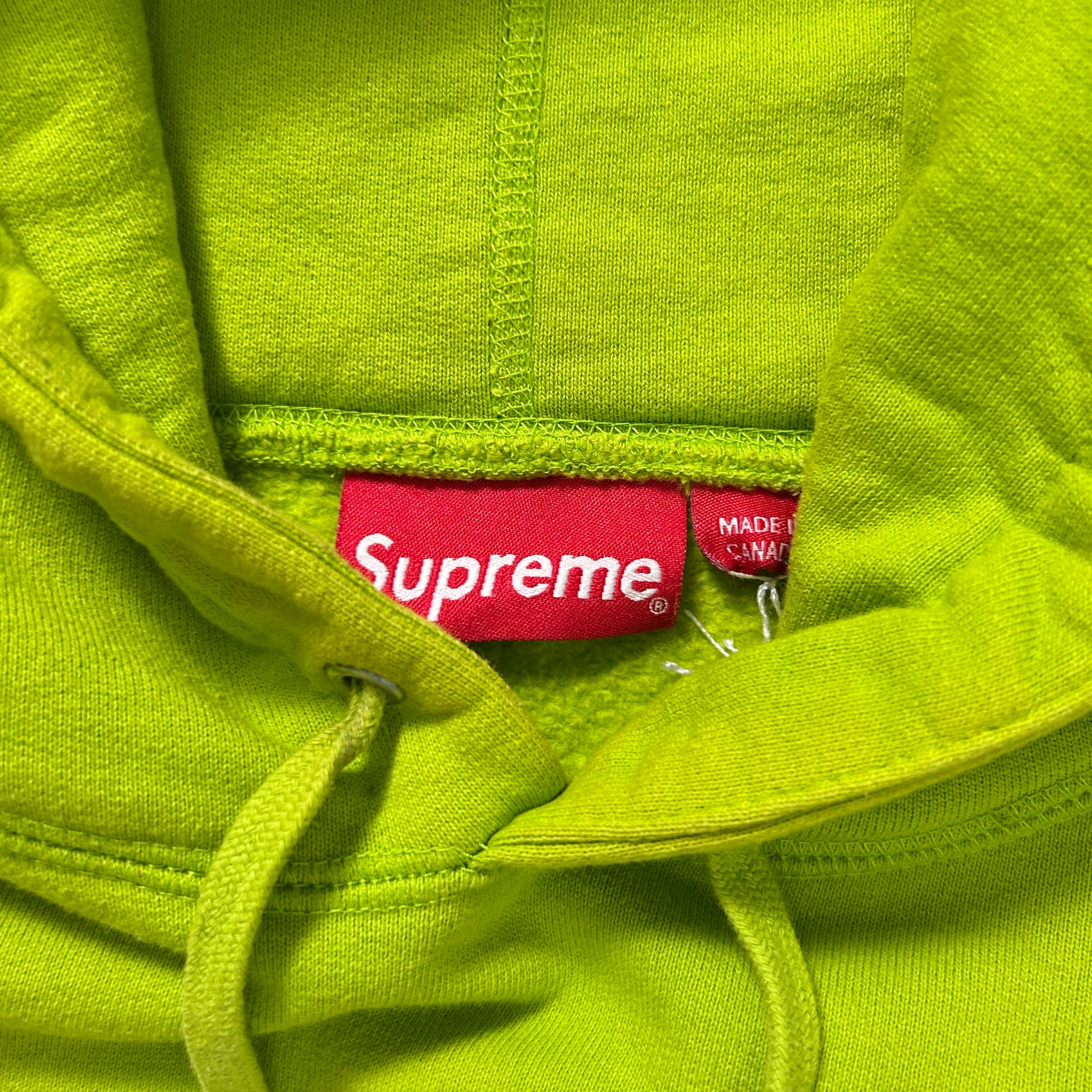 A bright lime green sweatshirt with a red Supreme logo and a red tag indicating it is made in Canada.