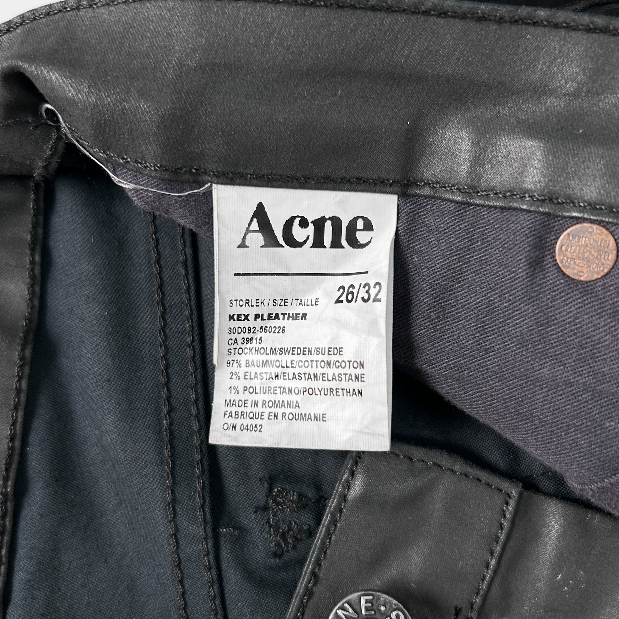 a close-up view of a black leather item, possibly a pair of pants or a jacket, with a label attached to it. The label appears to be a description or information about the item, such as the brand, size, material, and production location.