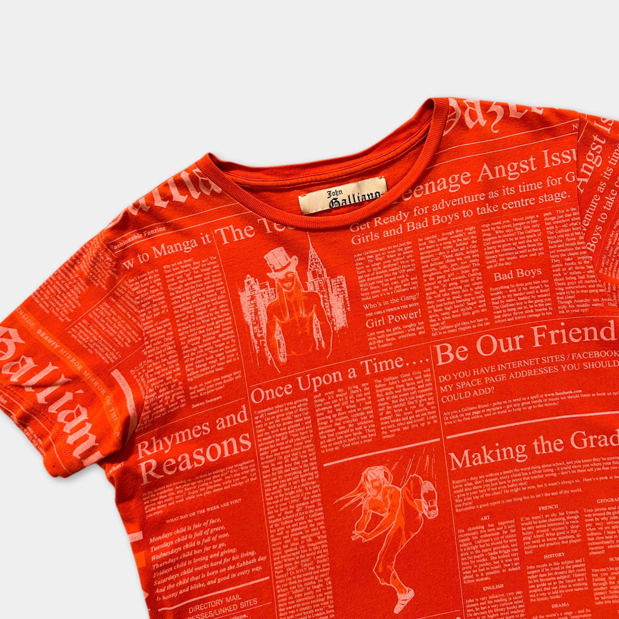 a bright orange t-shirt with a newspaper-style print on it. The print includes various headlines and articles, such as "Rhyme and Reason", "Once Upon a Time", and "Be Our Friend". The t-shirt appears to be a casual, everyday garment with a unique, eye-catching design.