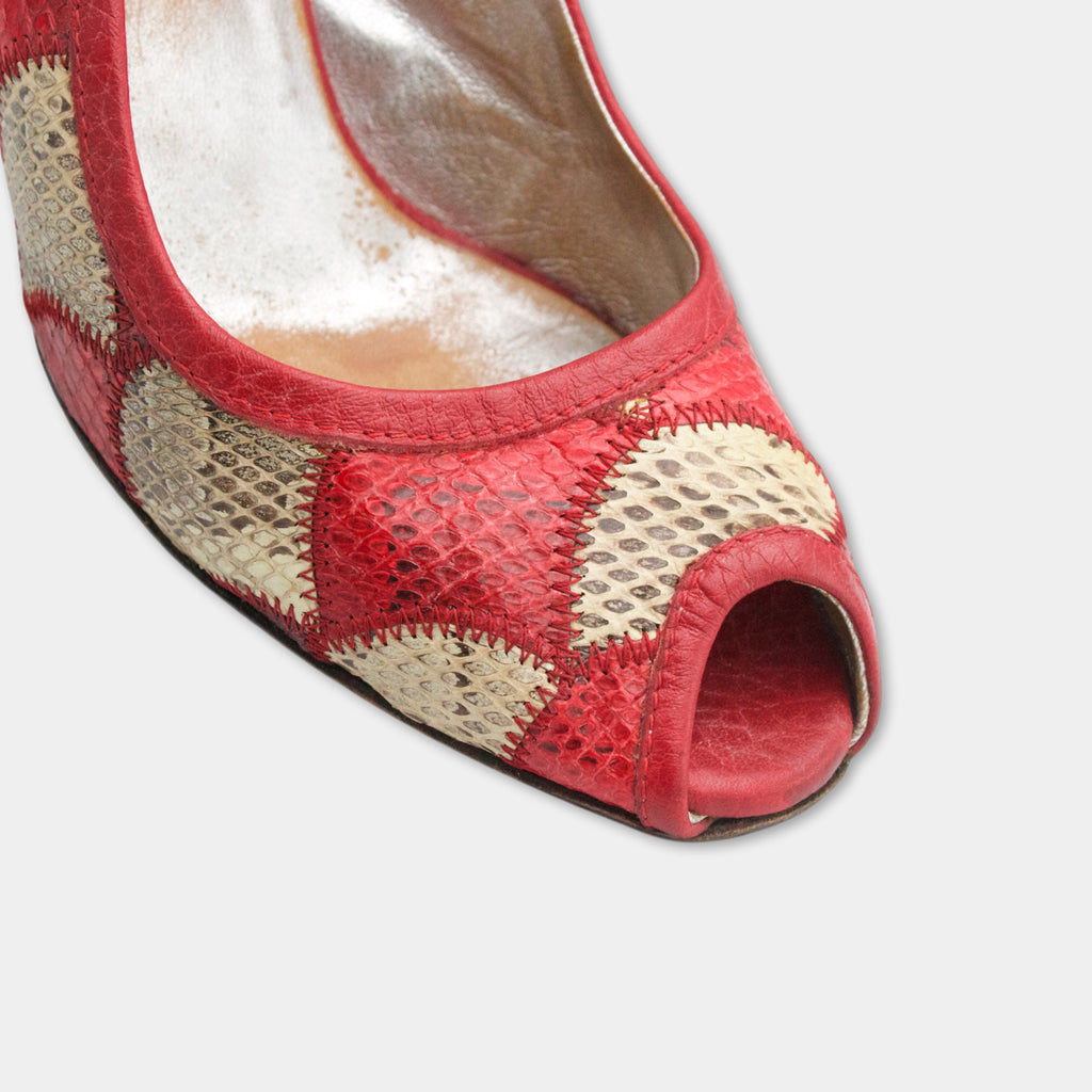A close-up view of a red and beige patterned shoe with a pointed toe and a small hole in the front.