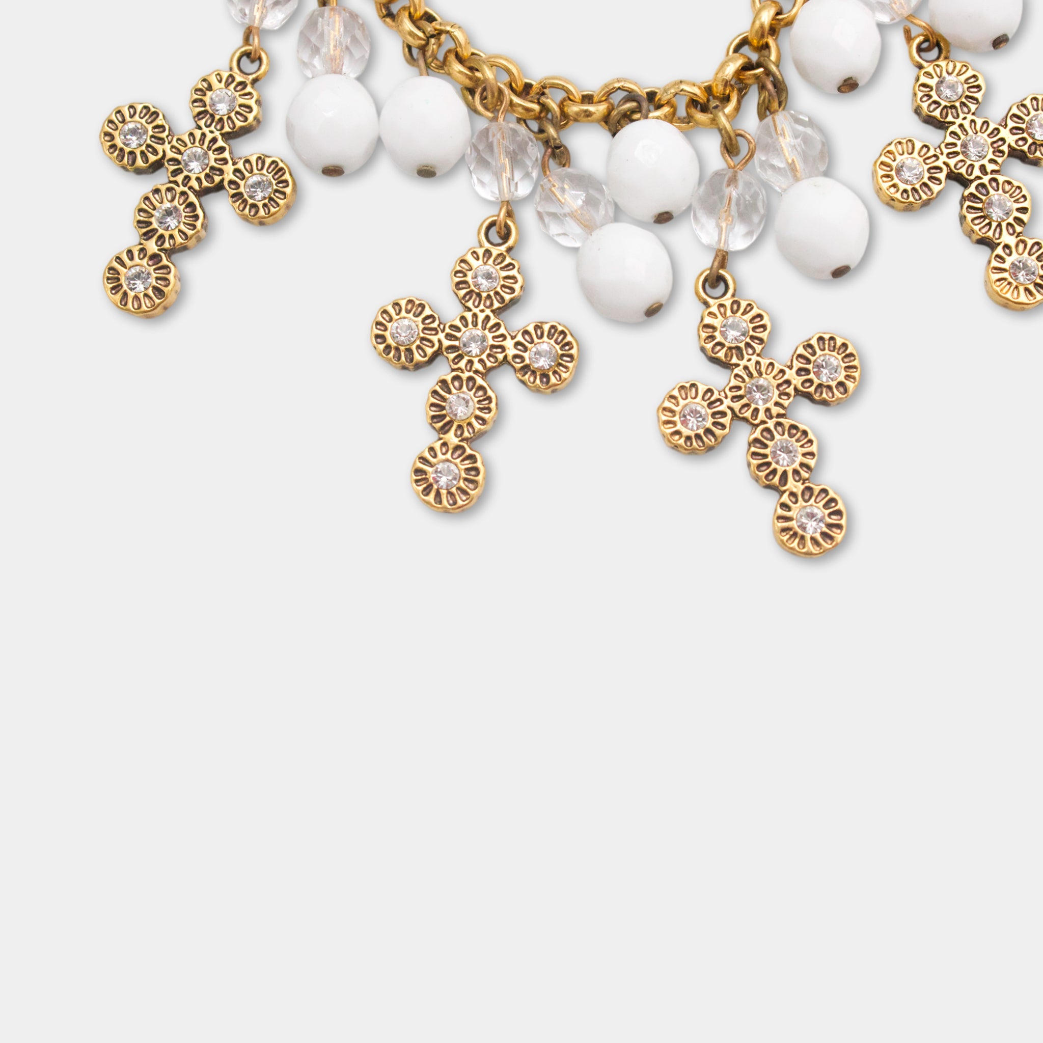 A close-up view of a gold cross-shaped charm bracelet adorned with white beads and clear gemstones.