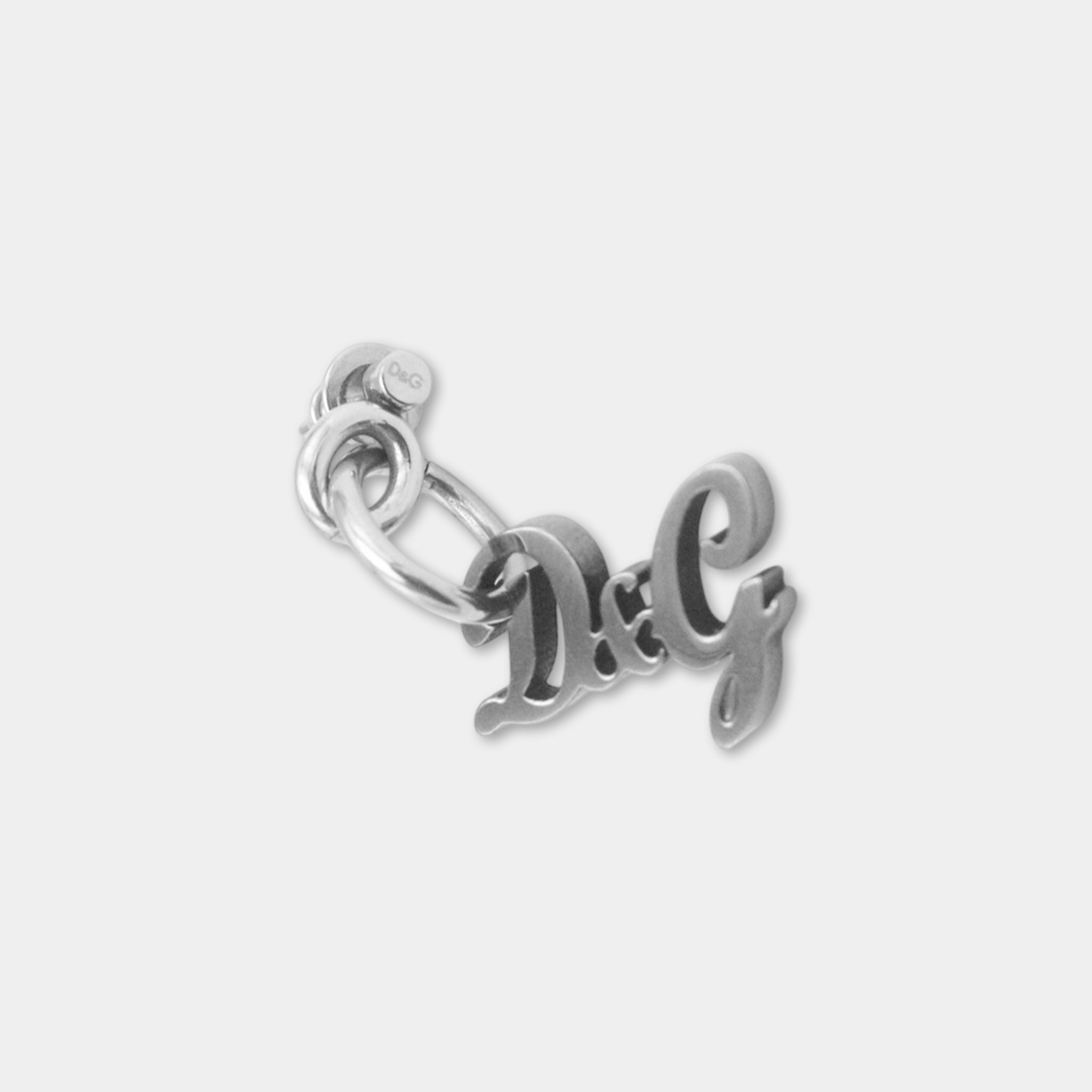 A silver-colored metal charm or keychain with the letters "D&G" engraved on it.