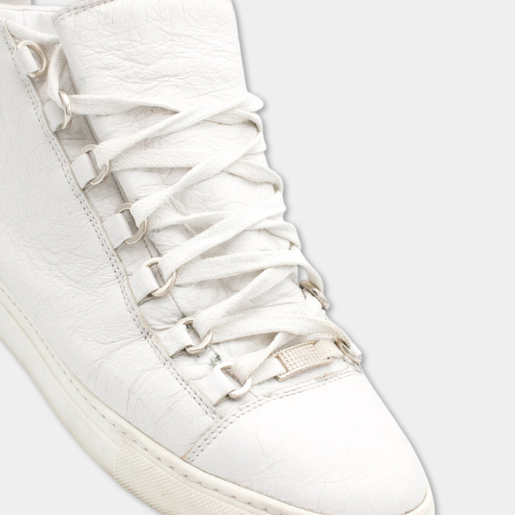 A close-up view of a white sneaker with a metal buckle on the side.