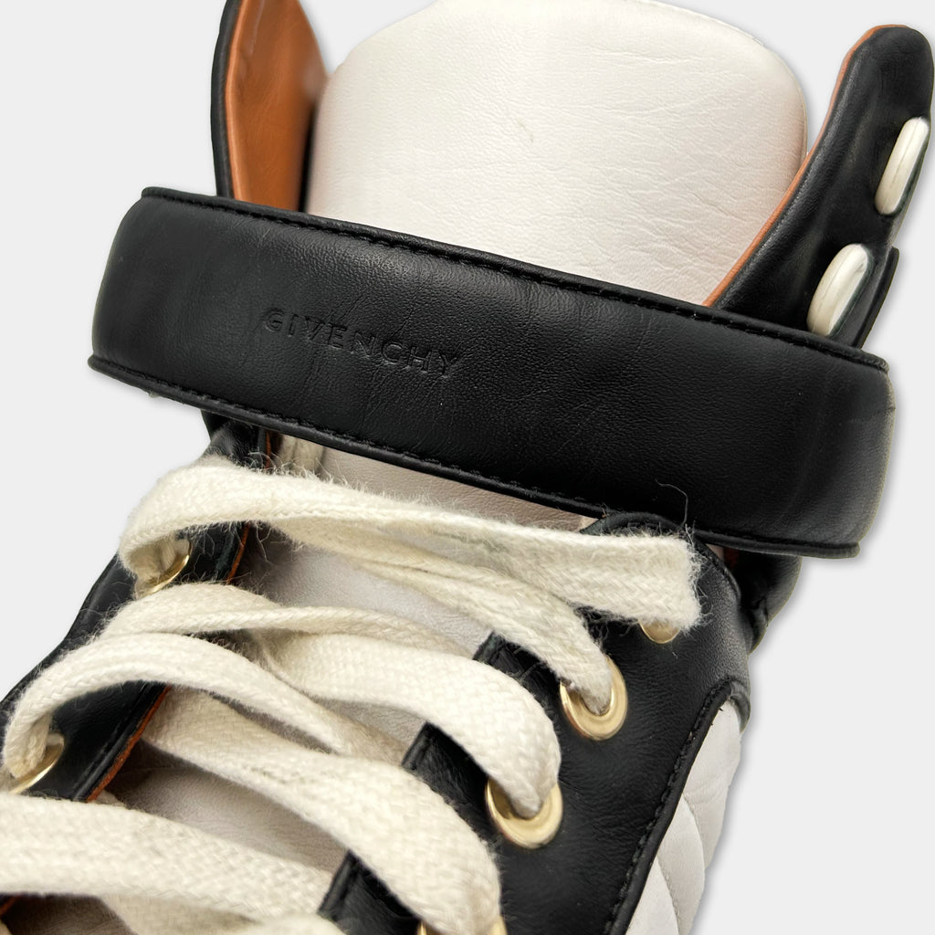 A close-up view of a black and white sneaker with a white lace and a black leather strap.