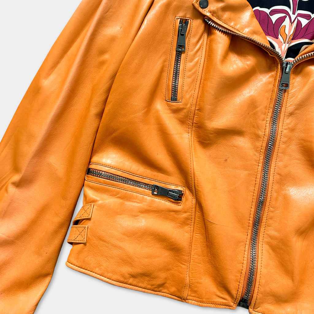 A close-up view of a bright orange leather jacket with multiple zippers and pockets.