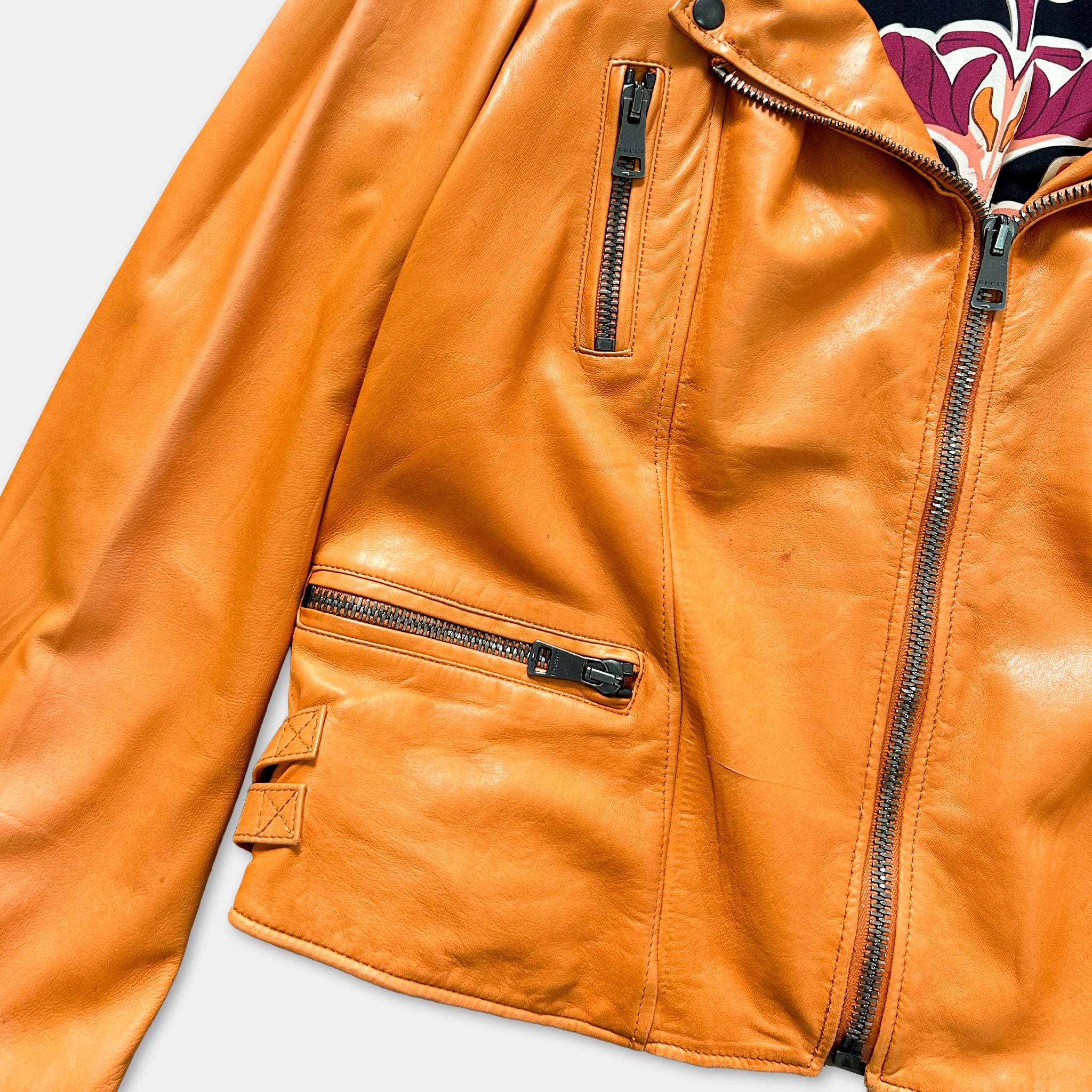 A close-up view of a bright orange leather jacket with multiple zippers and pockets.