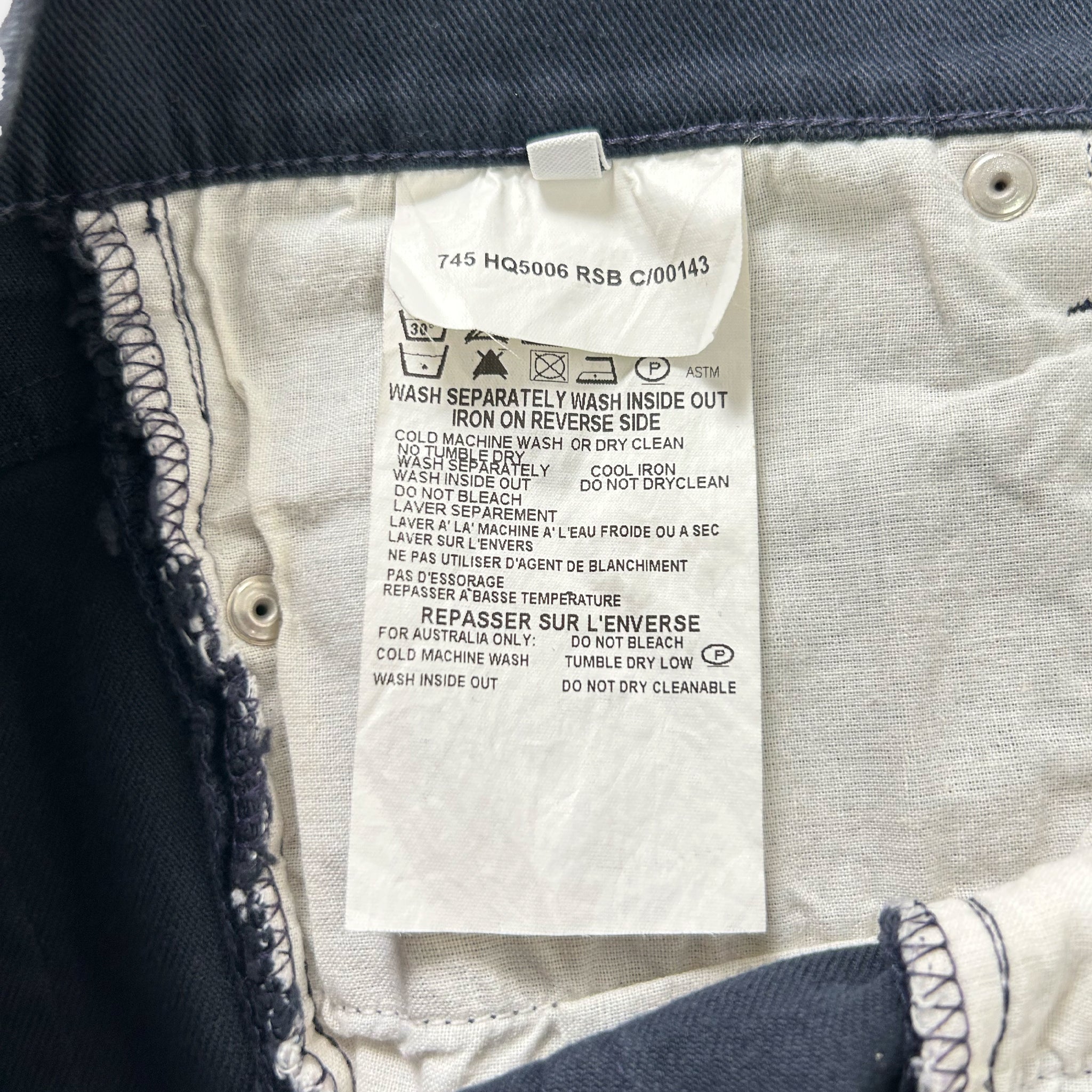 a close-up view of a white label on a pair of blue jeans, providing instructions on how to wash and care for the jeans.
