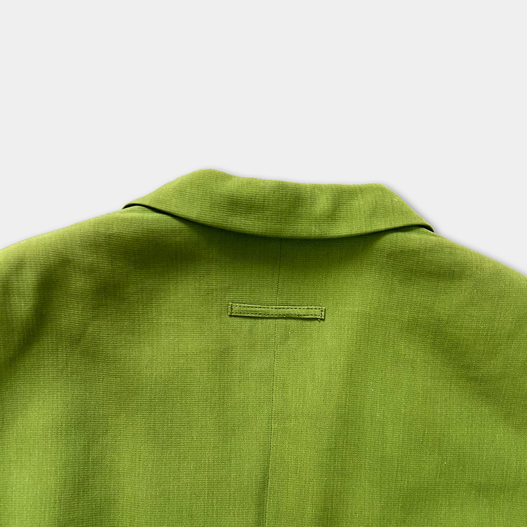 the back of a bright green jacket or blazer, with a small label or patch visible on the fabric.