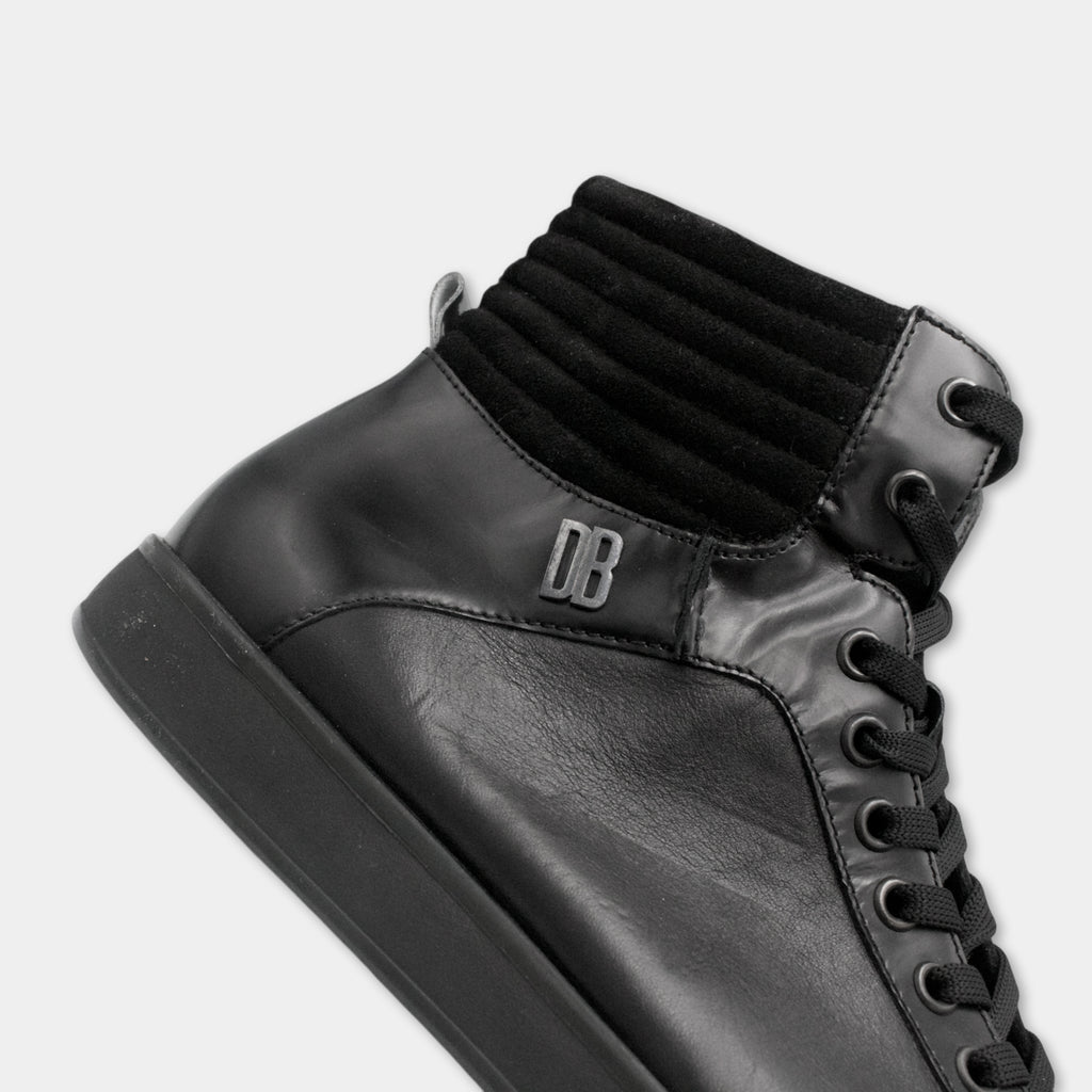 A close-up view of a black leather shoe with a thick, textured sole and a black lace-up closure.