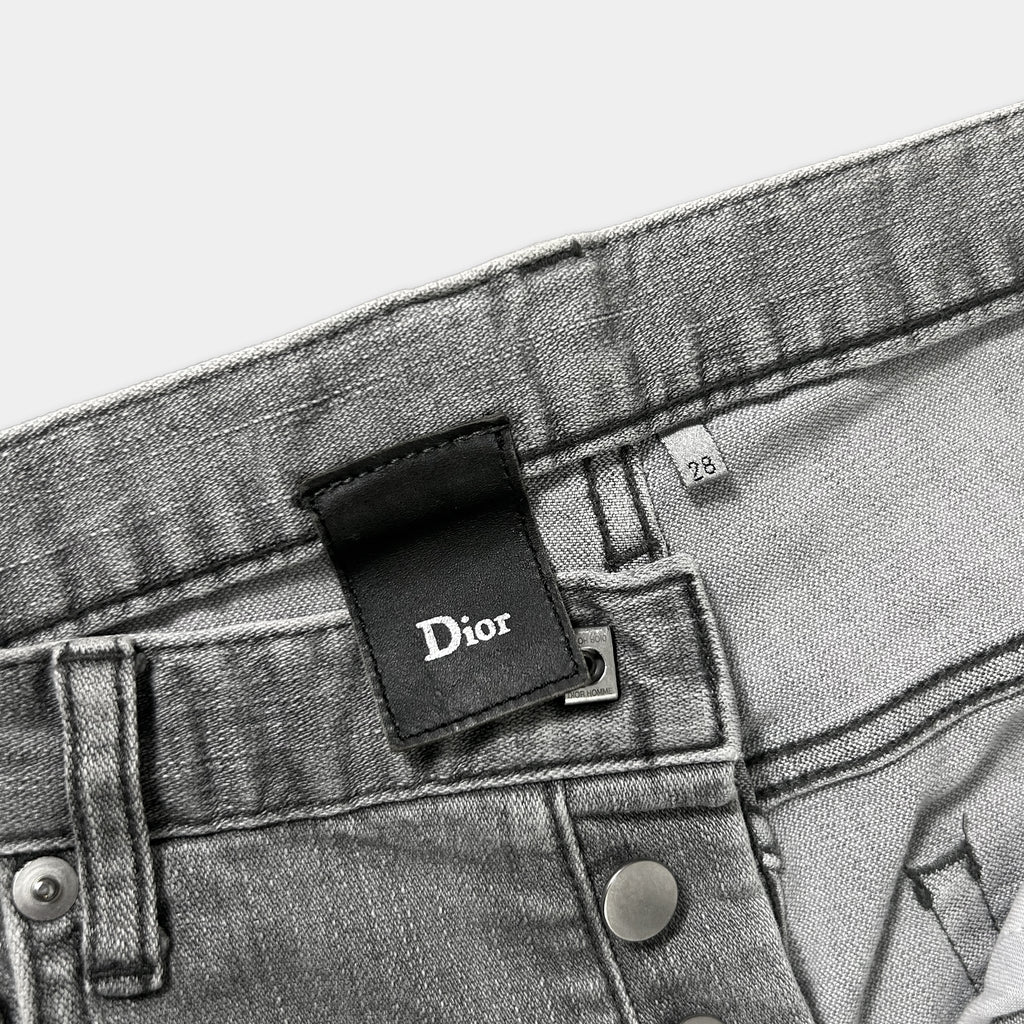 A close-up view of a pair of gray denim jeans, with a Dior brand label attached to the waistband.