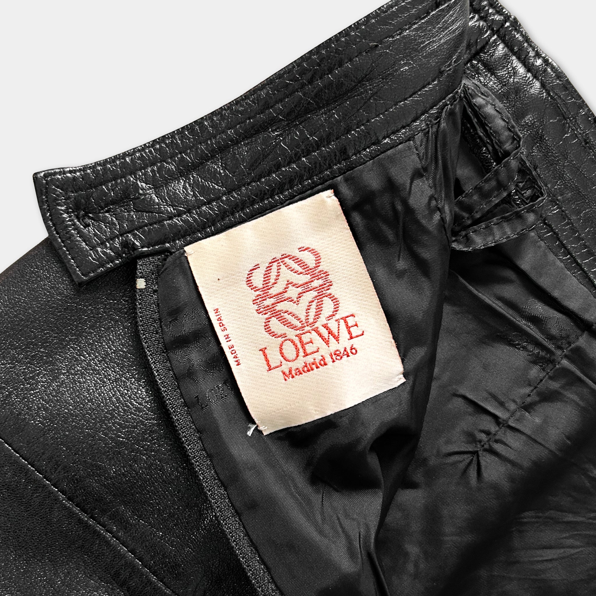 A close-up view of a black leather jacket with a red and white LOEWE tag attached to the collar.