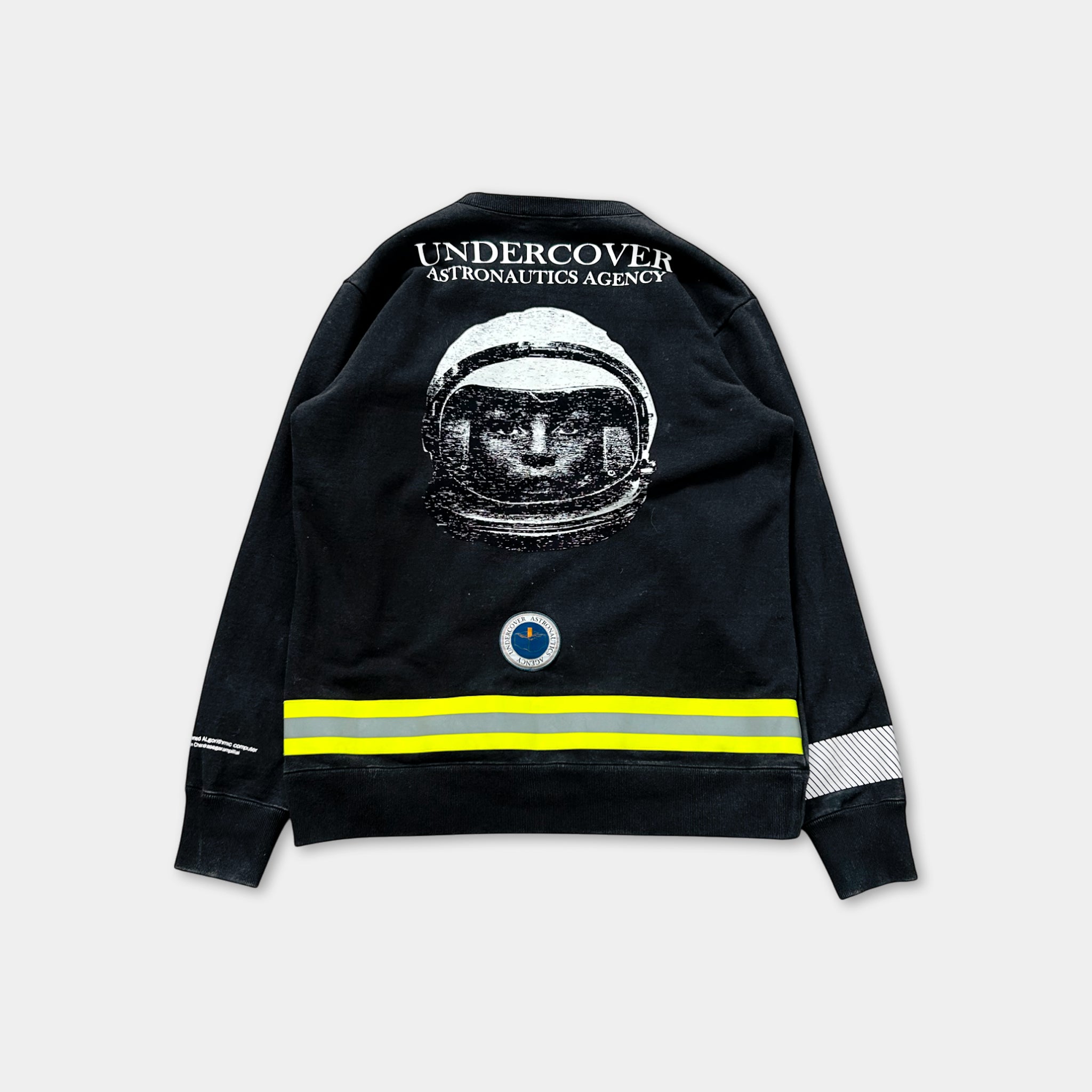 a black sweatshirt with a graphic of a person wearing a spacesuit and the text "Undercover Astronautics Agency" printed on the back.