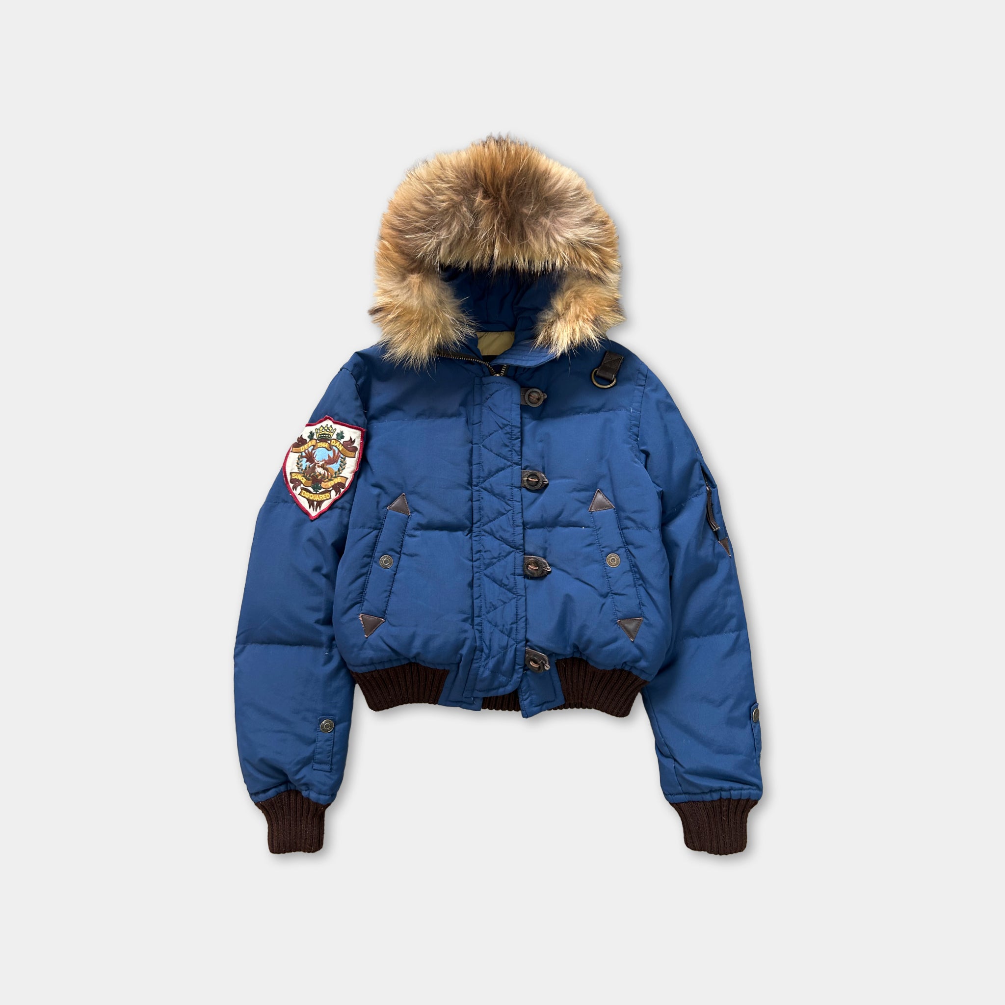 A blue puffy jacket with a fur-trimmed hood, featuring a patch on the left side and buttons on the front.