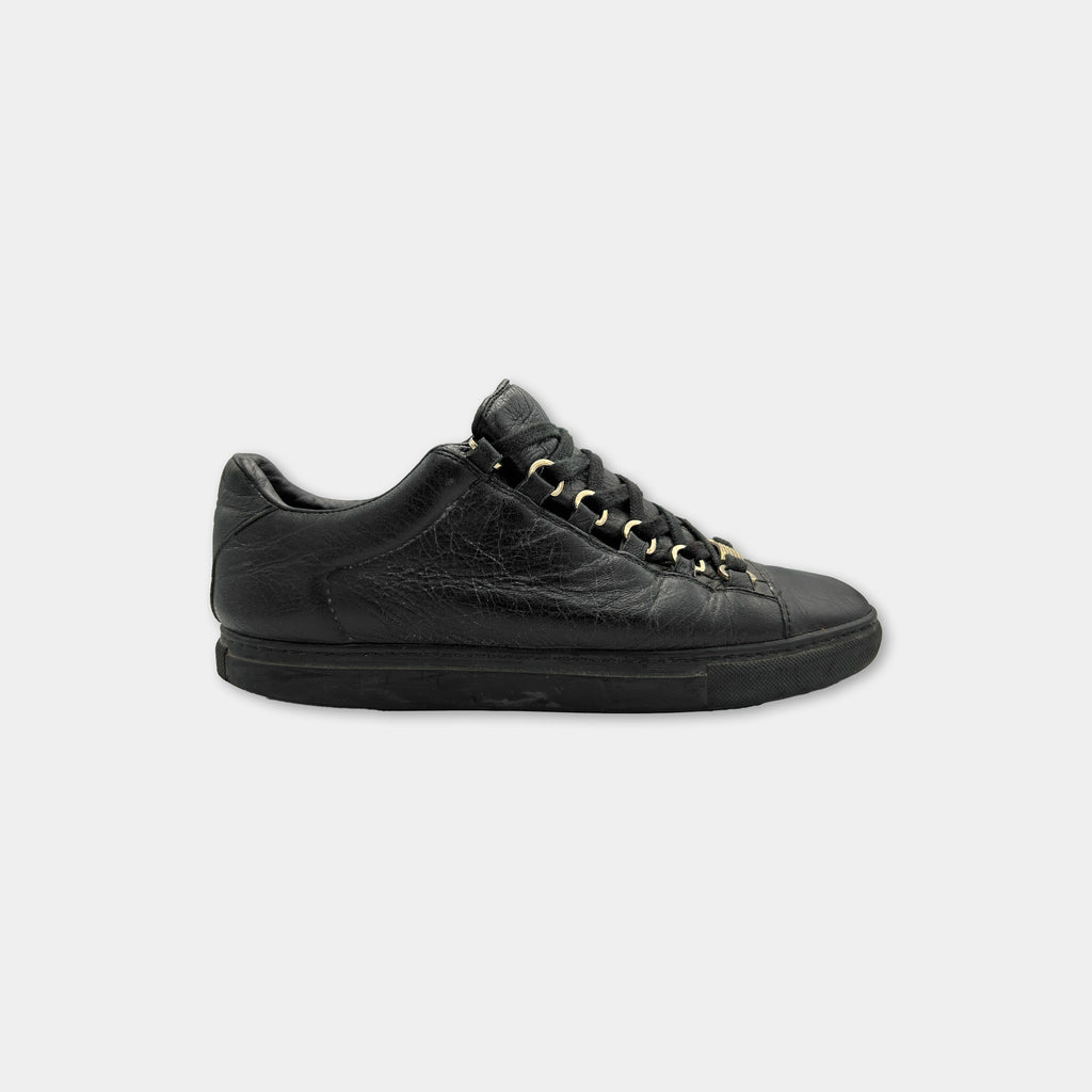 A black leather sneaker with gold-colored laces and a black sole.