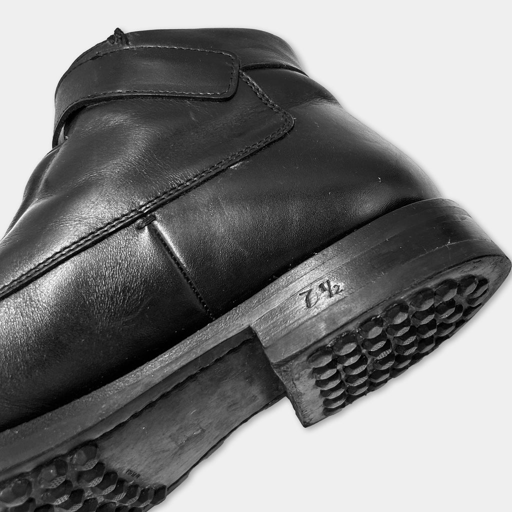 A close-up black and white image of a black leather boot with a sole and heel.