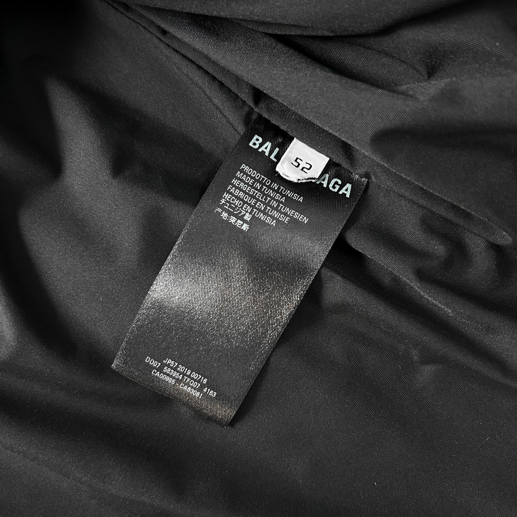a close-up view of a black fabric, possibly a garment or textile, with a label attached to it. The label appears to be a product label from a brand like Balenciaga, providing information about the product.