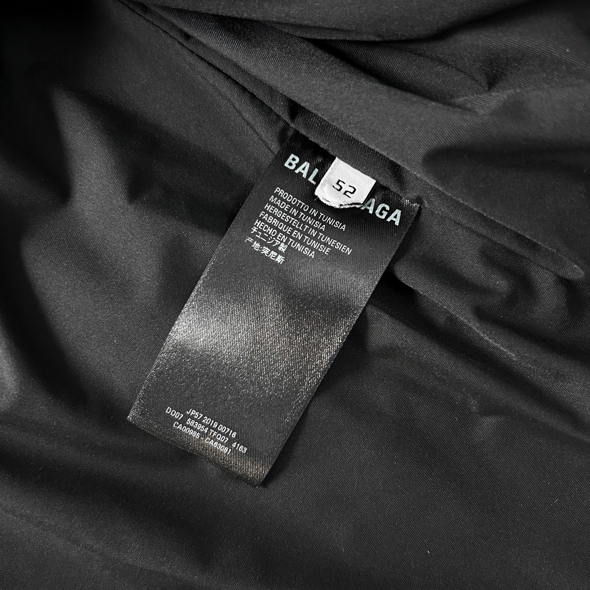 a close-up view of a black fabric, possibly a garment or textile, with a label attached to it. The label appears to be a product label from a brand like Balenciaga, providing information about the product.
