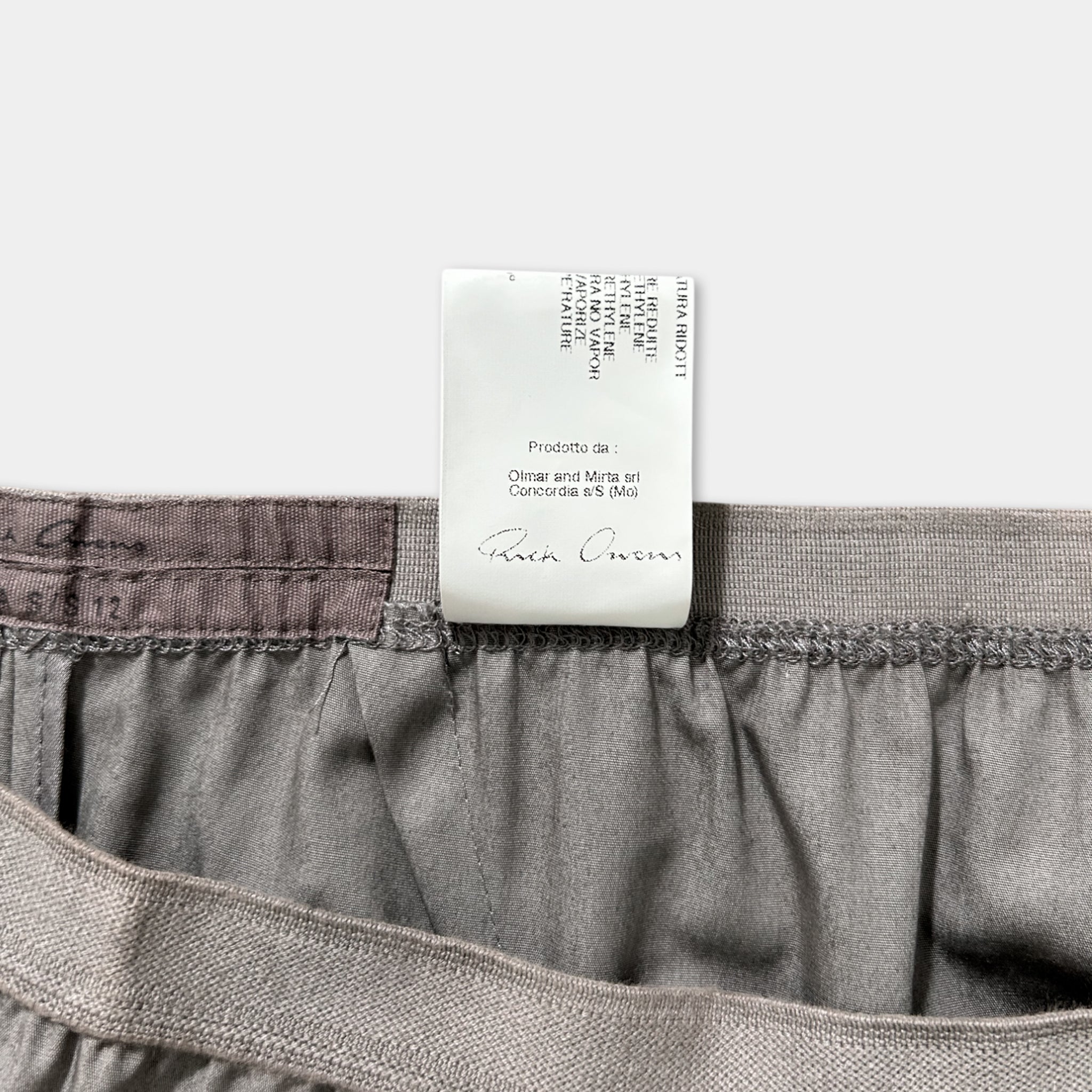 a close-up view of a gray garment, possibly a pair of pants or shorts, with a label attached to it. The label appears to be a product label or tag, providing information about the garment.
