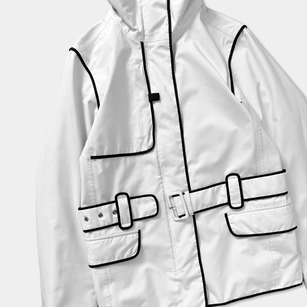 A white jacket with black trim and buckles, featuring a front pocket and a belt detail.