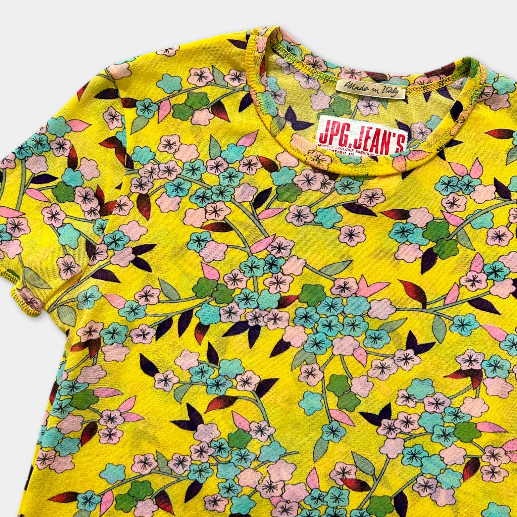 A yellow floral print shirt with a collar and tag, featuring a variety of colorful flowers and leaves.
