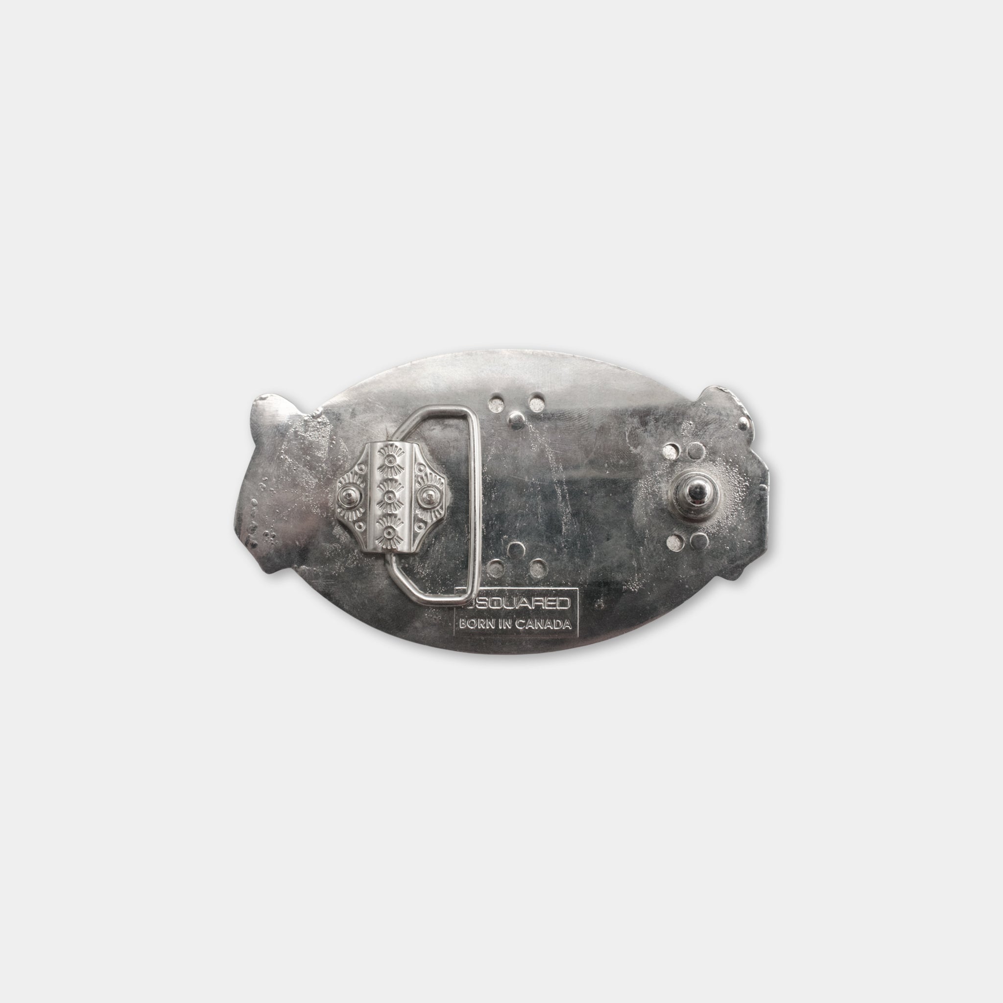a silver-colored metal object, possibly a belt buckle or a similar accessory, with a decorative design and some text on it.