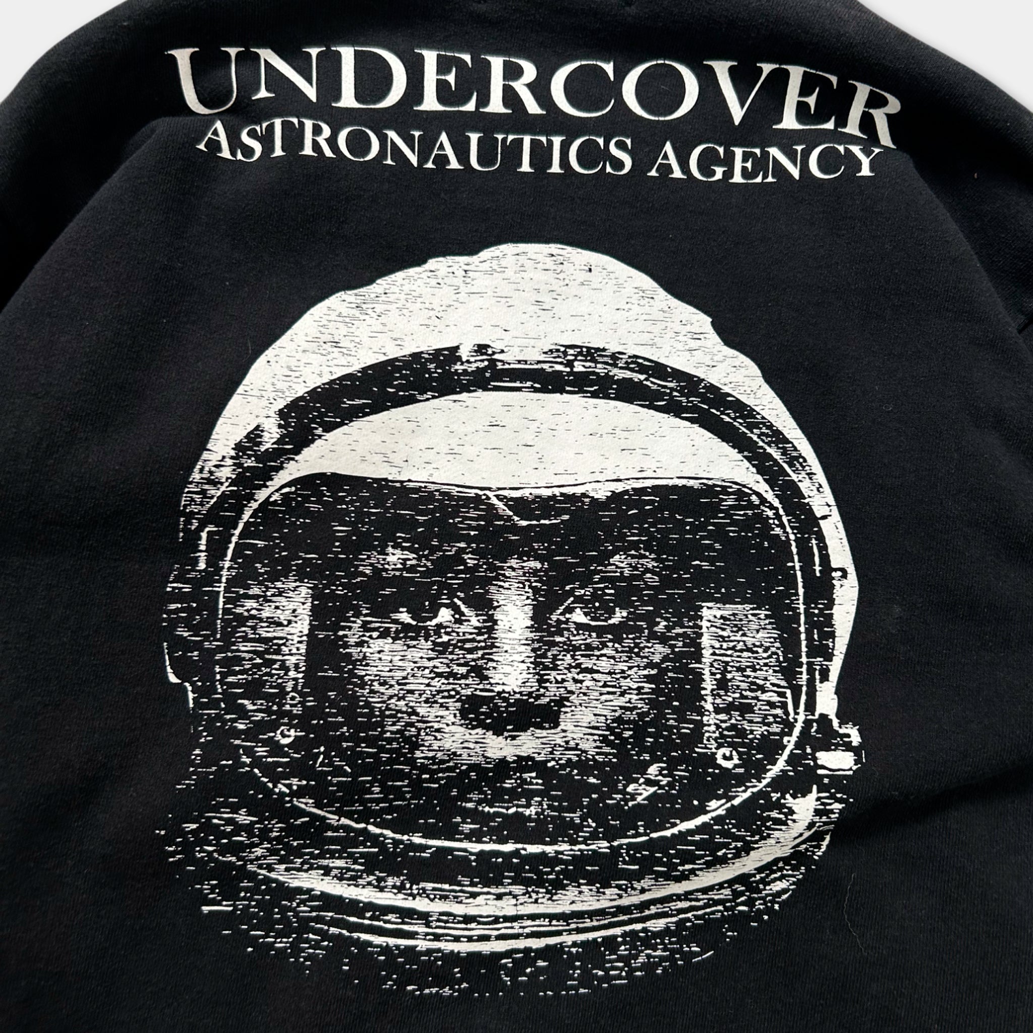 a black and white graphic of a space helmet with the text "Undercover Astronautics Agency" printed on the back of a black shirt.