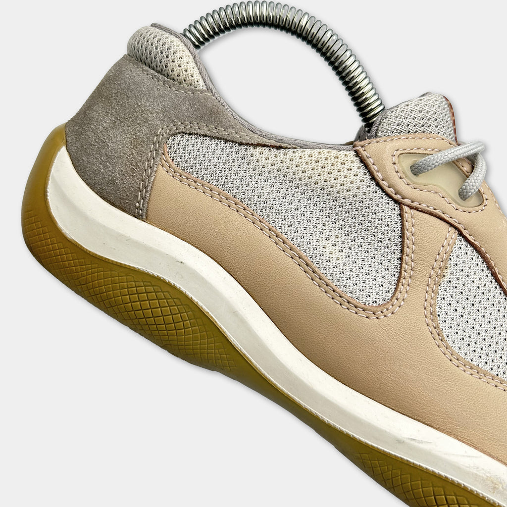 A close-up view of a beige and gray athletic shoe with a metal coiled shoe holder attached to the side.