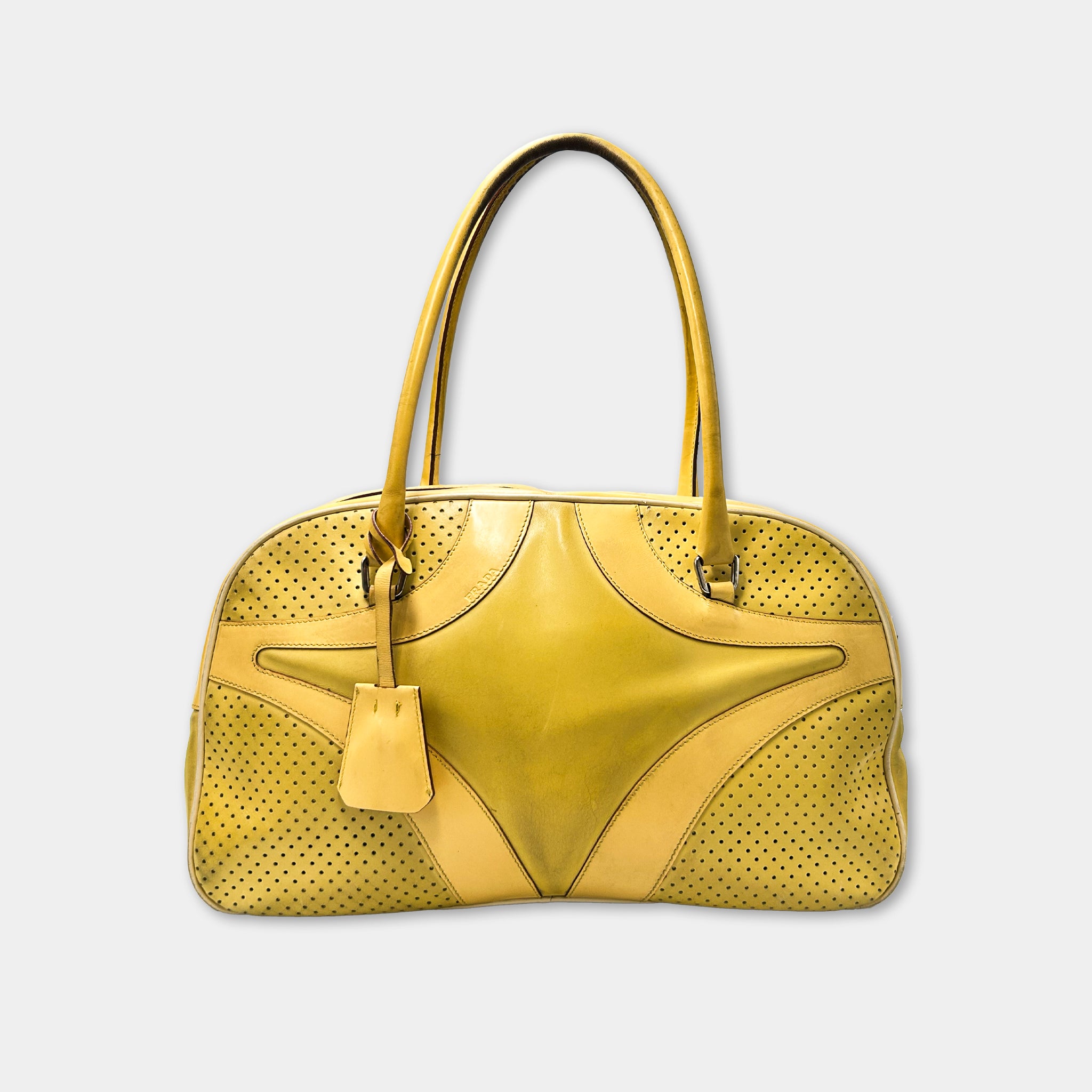 A yellow handbag with a perforated pattern and a small tag attached to it.