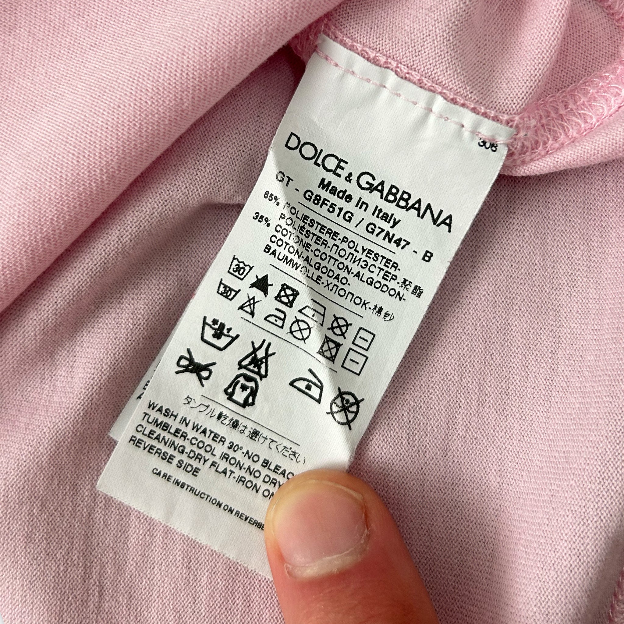 A close-up view of a white label with text and symbols on a pink fabric, held by a person's thumb.