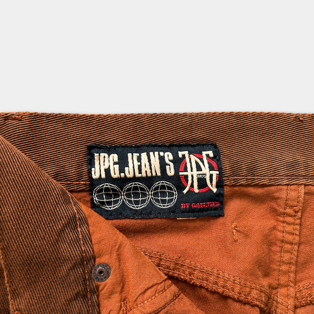 a close-up view of a brown pair of jeans, with a label attached to the waistband that reads "JPG.Jean's JPC".