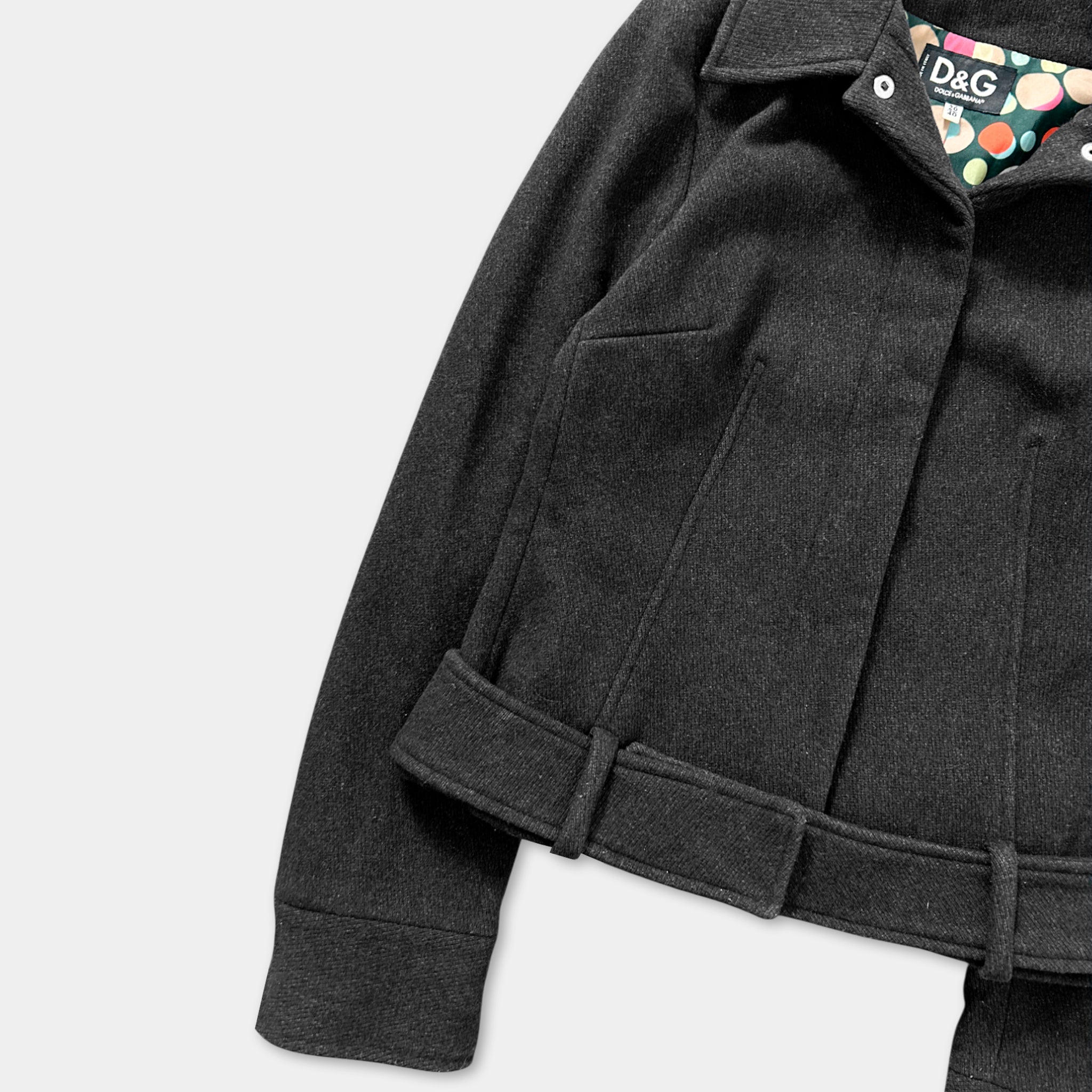 A close-up view of a black coat with a collar and a patterned patch on the left side.