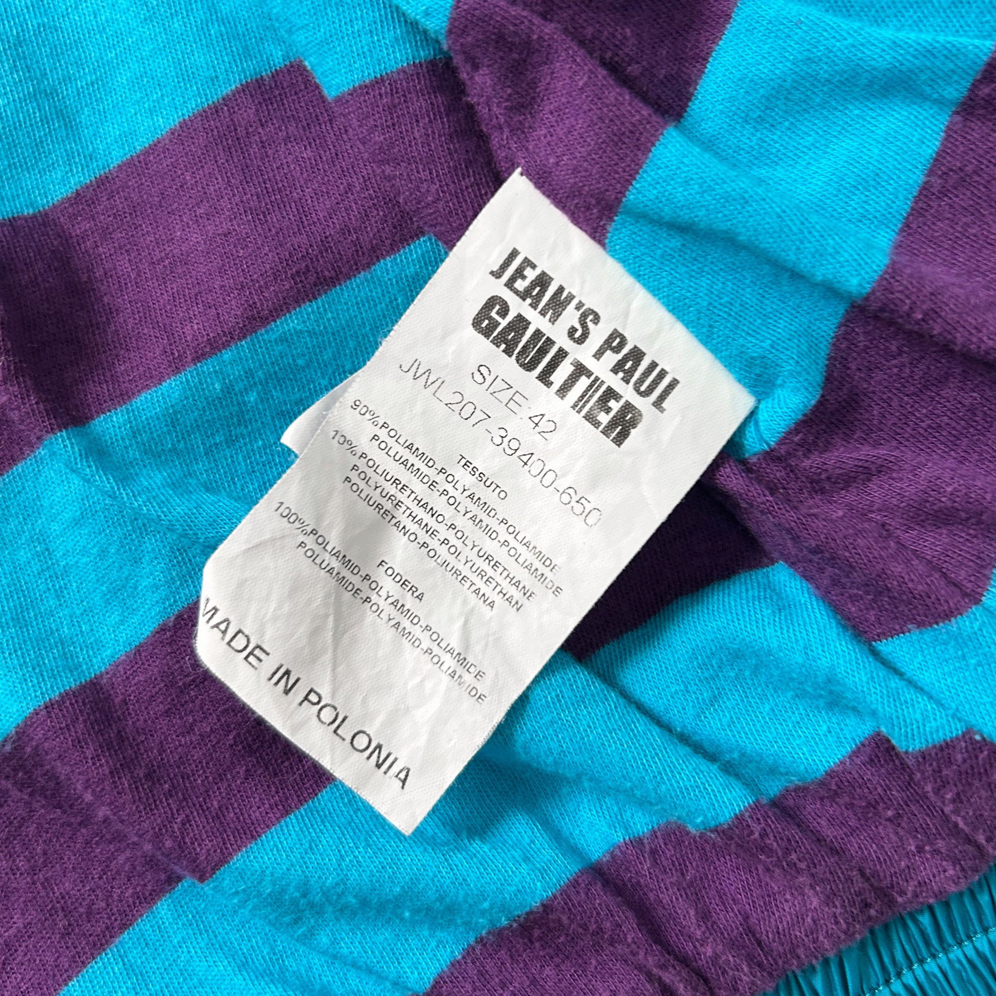 A close-up of a fabric label with text, placed on a fabric with a purple and blue striped pattern.