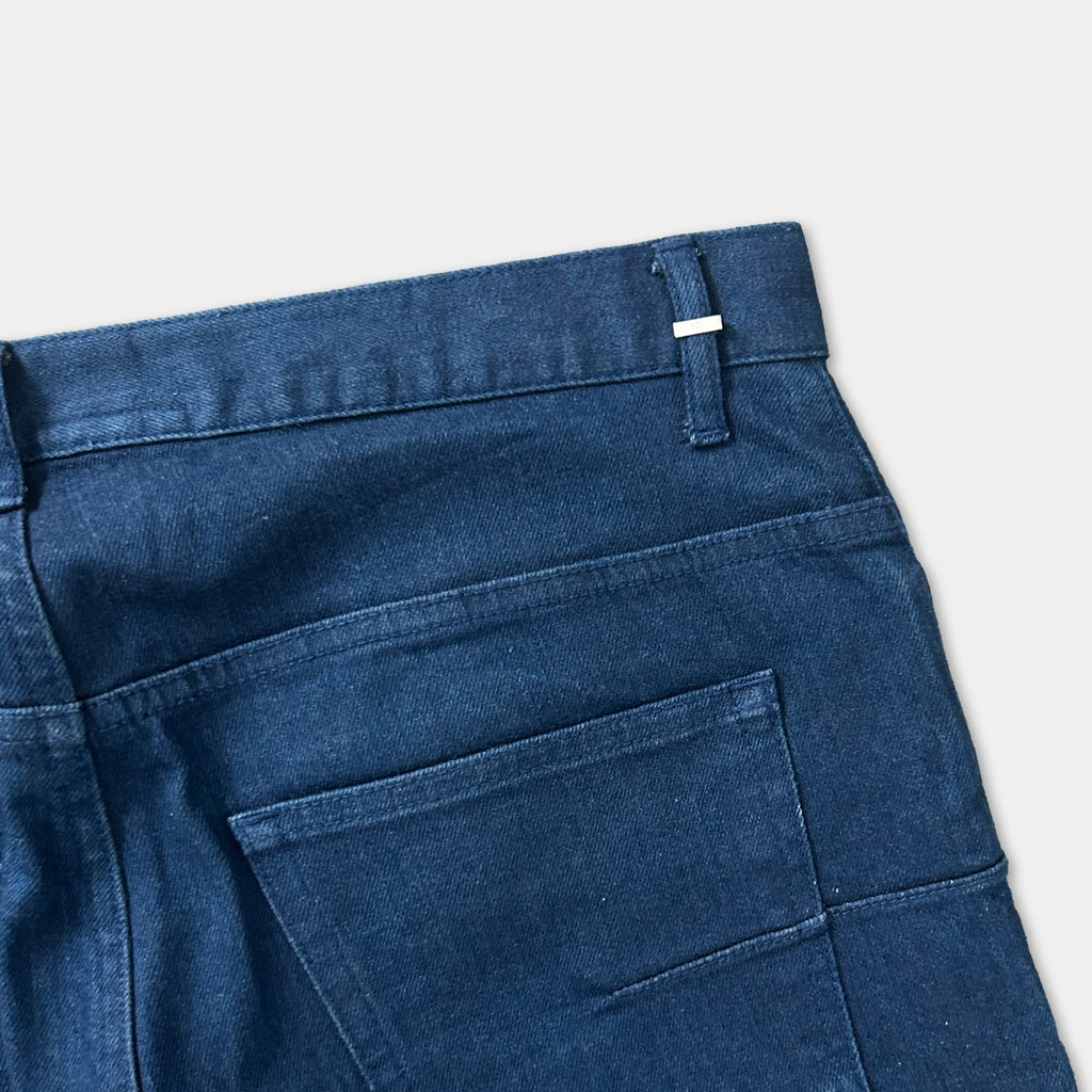 A close-up view of a pair of blue jeans, showing the waistband and pocket.