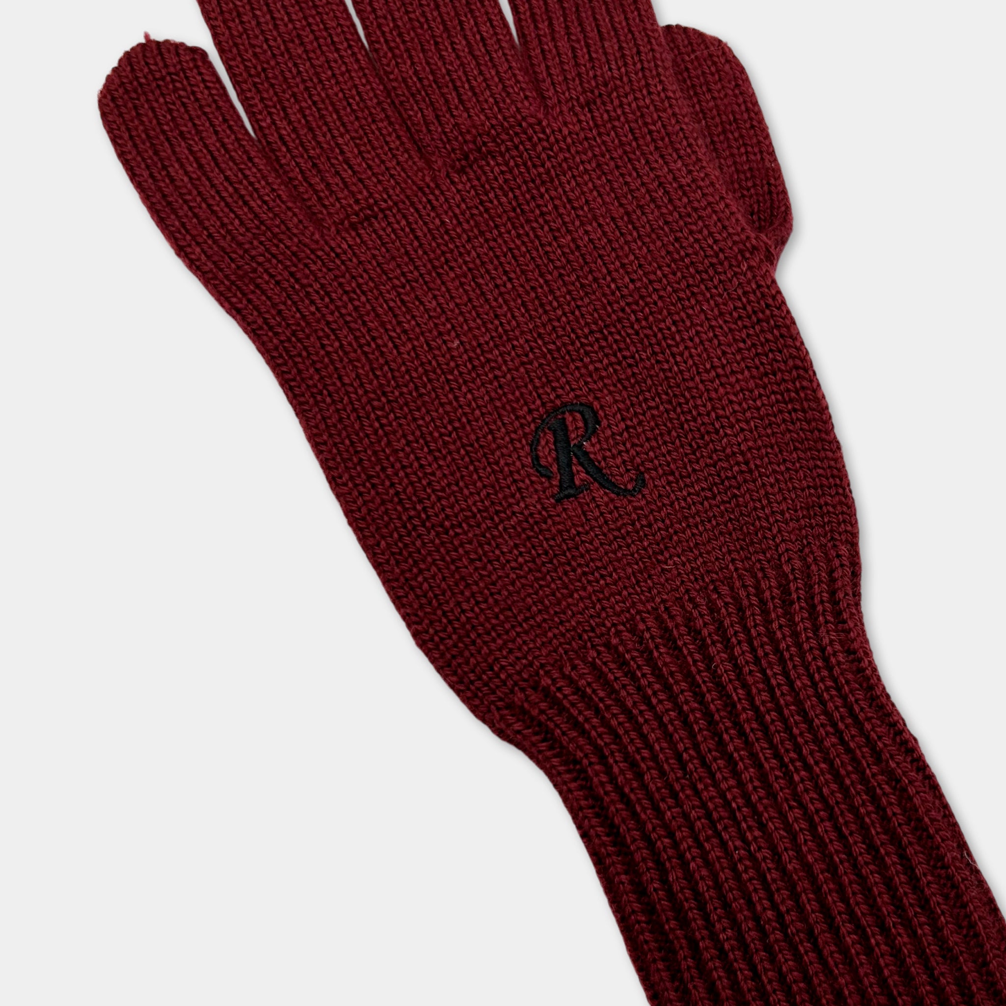 A burgundy knitted glove with a black "R" logo on the palm.