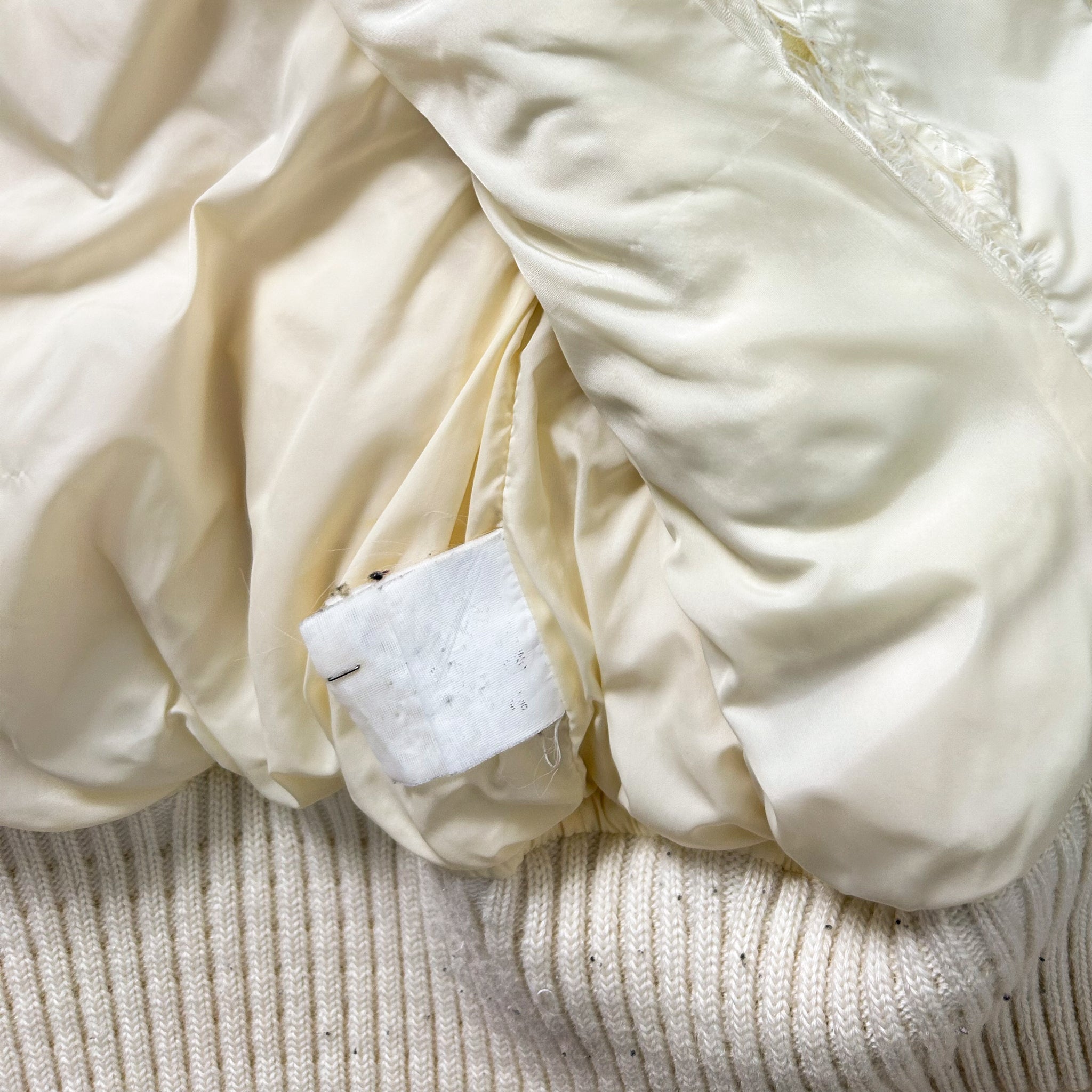a close-up view of a white fabric, possibly a blanket or garment, with a small white label attached to it.