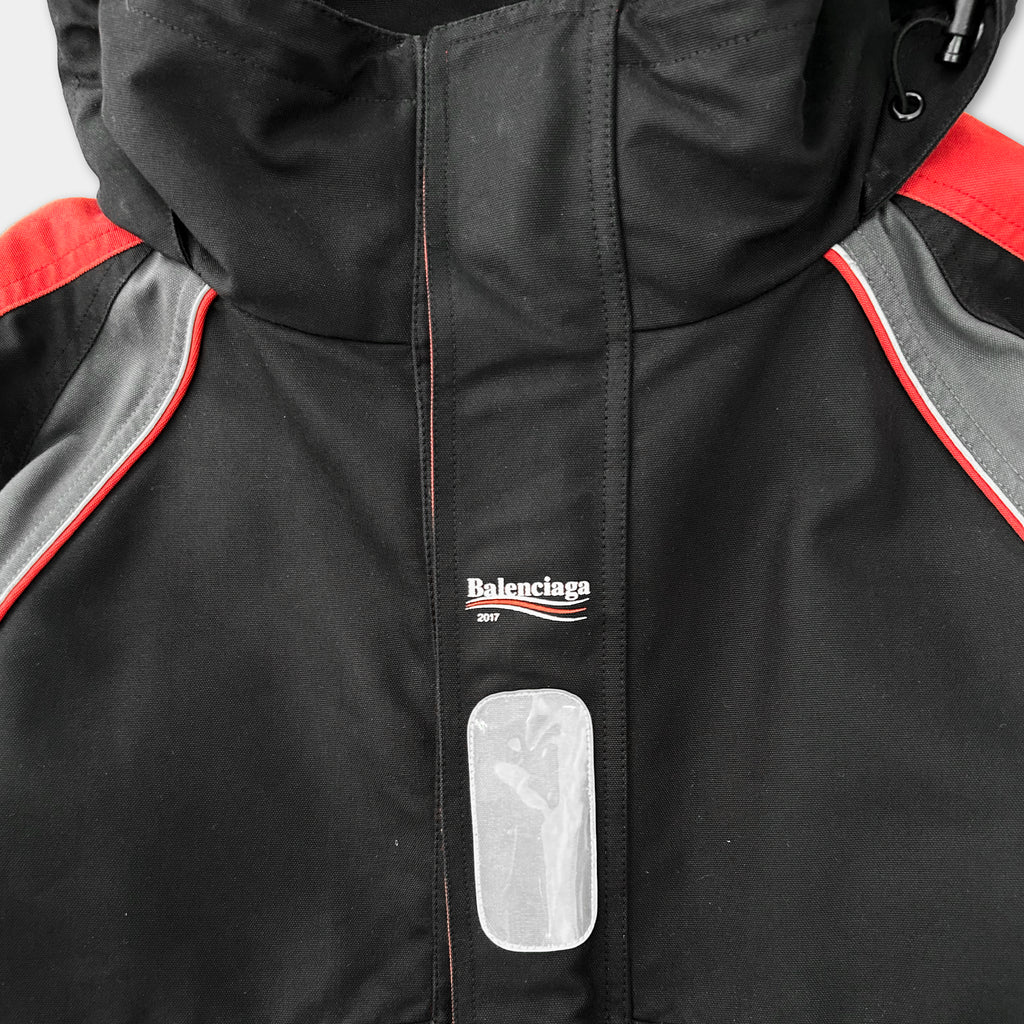 A close-up view of a black and red jacket with a Balenciaga logo and a small white patch on the front.