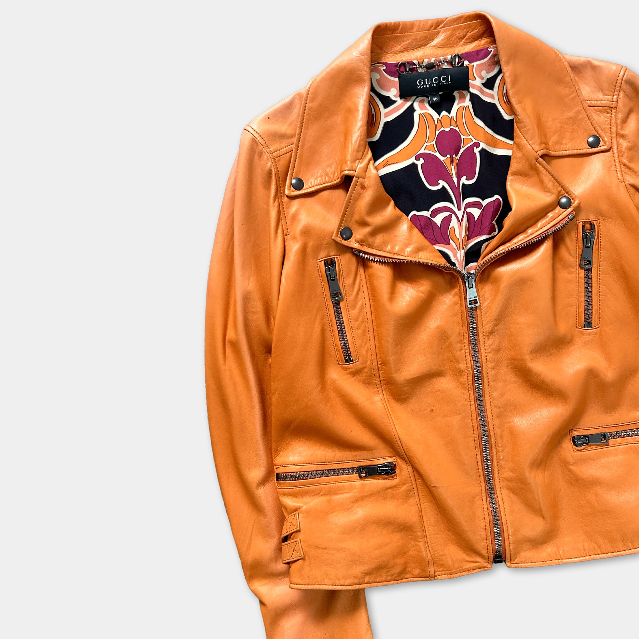 A bright orange leather jacket with a floral pattern on the inside lining.