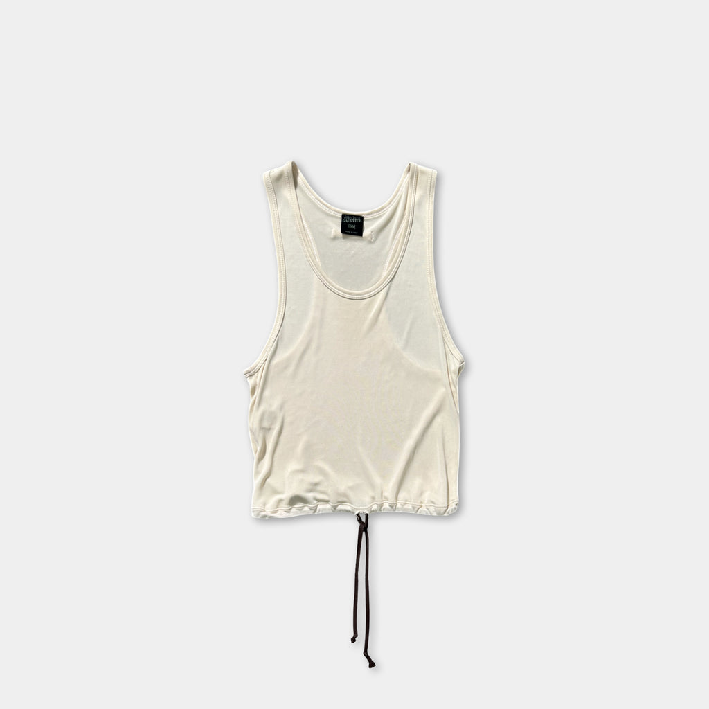 A white tank top with a drawstring waist and a black tie at the bottom is shown against a plain white background.