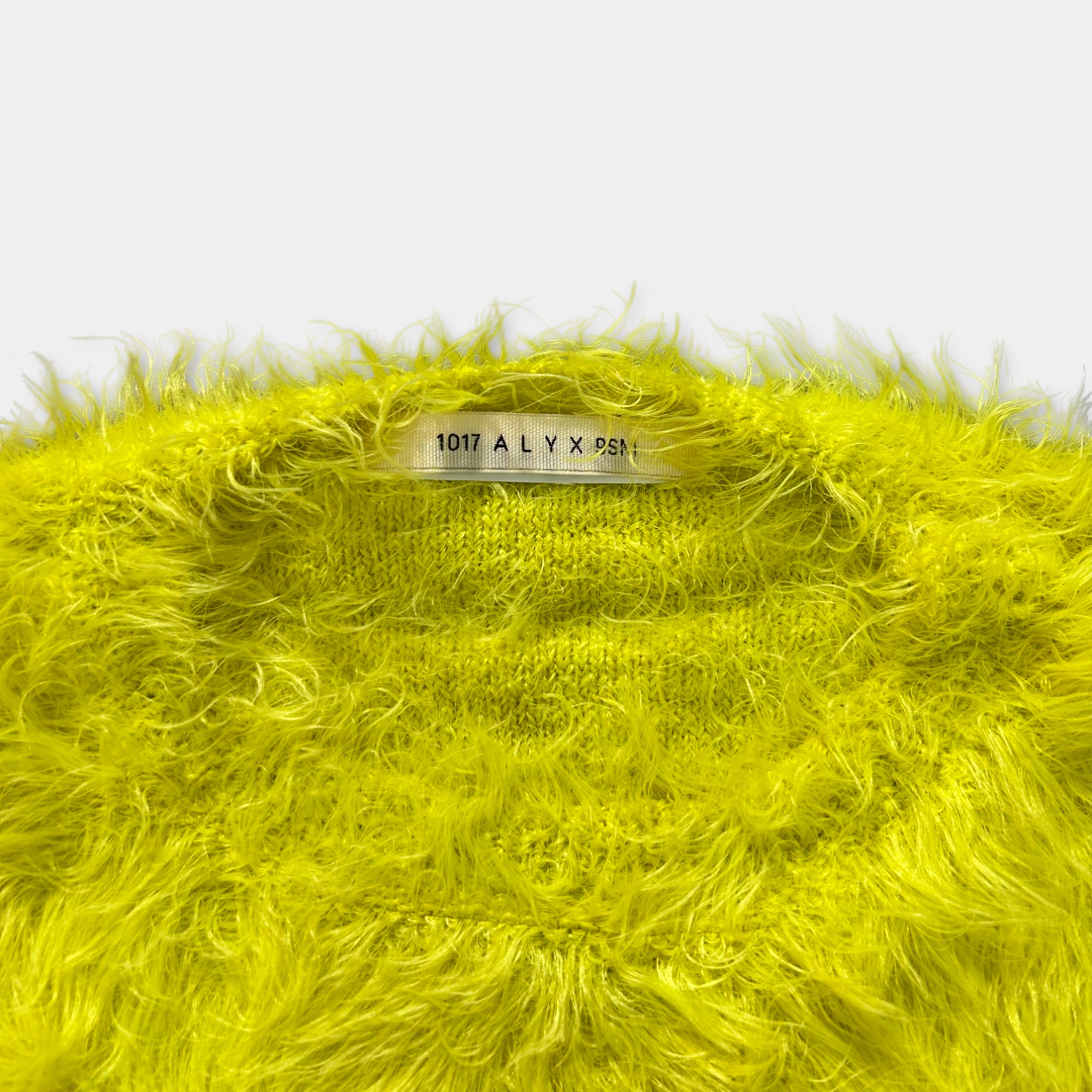 A bright yellow fuzzy sweater with a label on the collar.