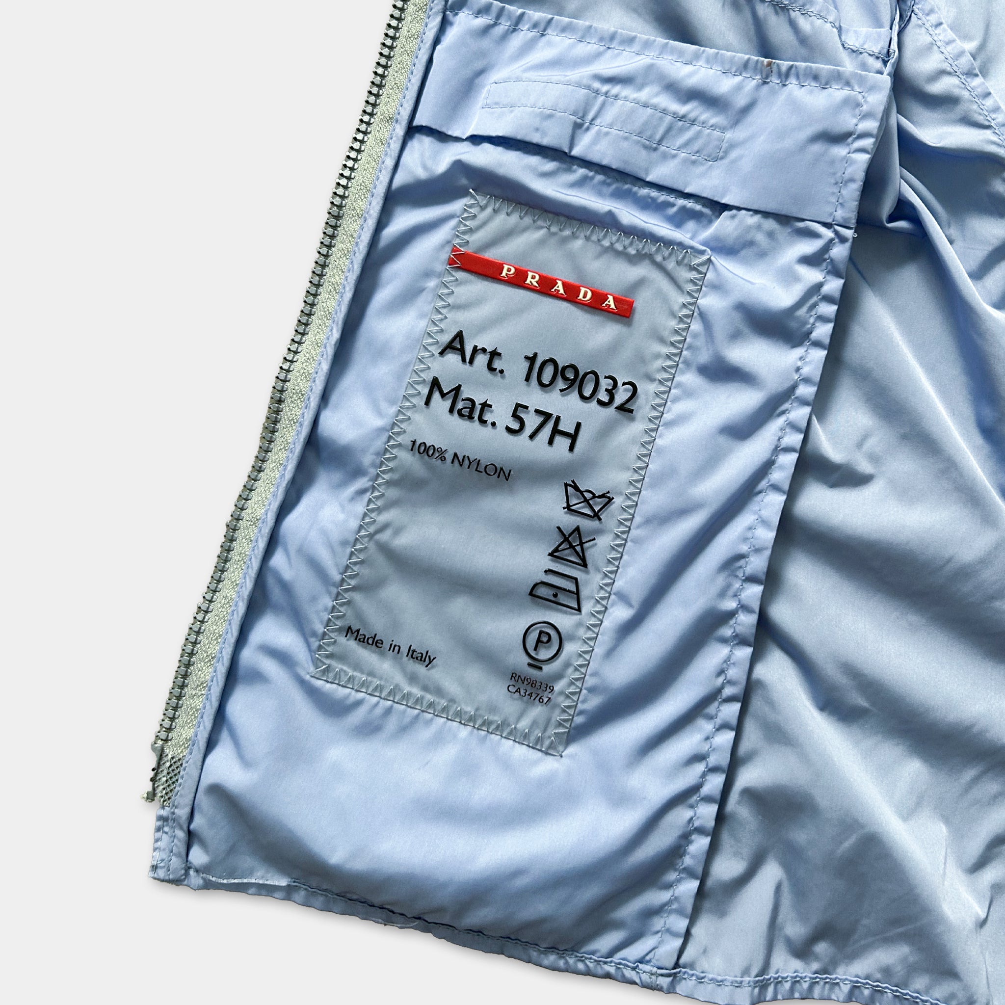 a close-up view of a blue jacket with a label on the pocket, which appears to be a Prada product.