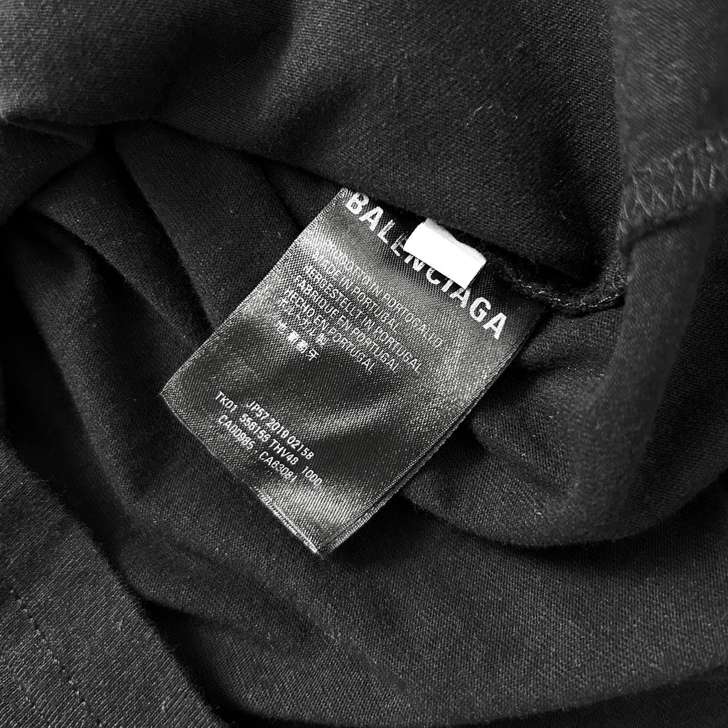 A close-up black and white image of a fabric label with text, likely a garment label from a clothing brand.