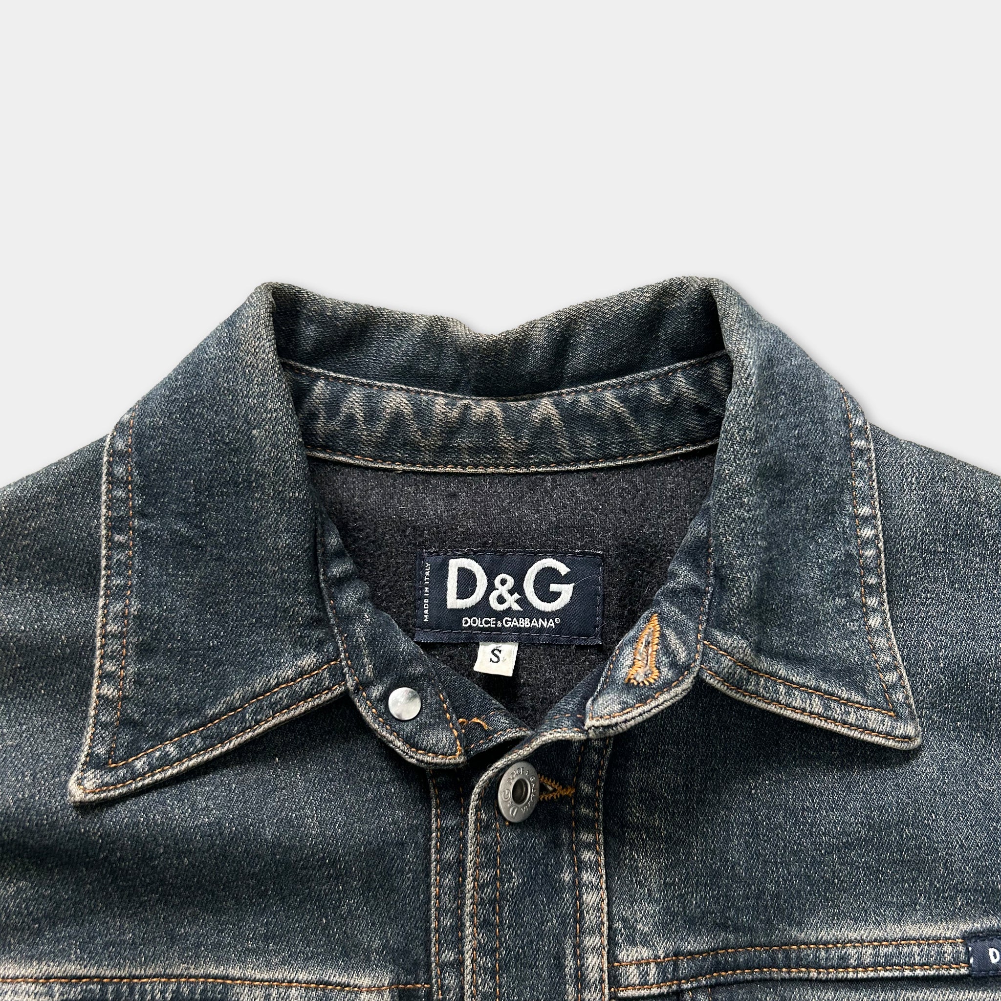 A close-up view of a denim jacket collar and buttons, with a label on the collar that reads "D&G".