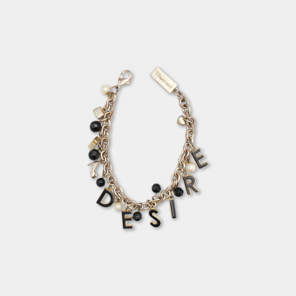 A bracelet with the word "DESIRE" spelled out in black letters, surrounded by various charms and beads in shades of black, white, and gold.