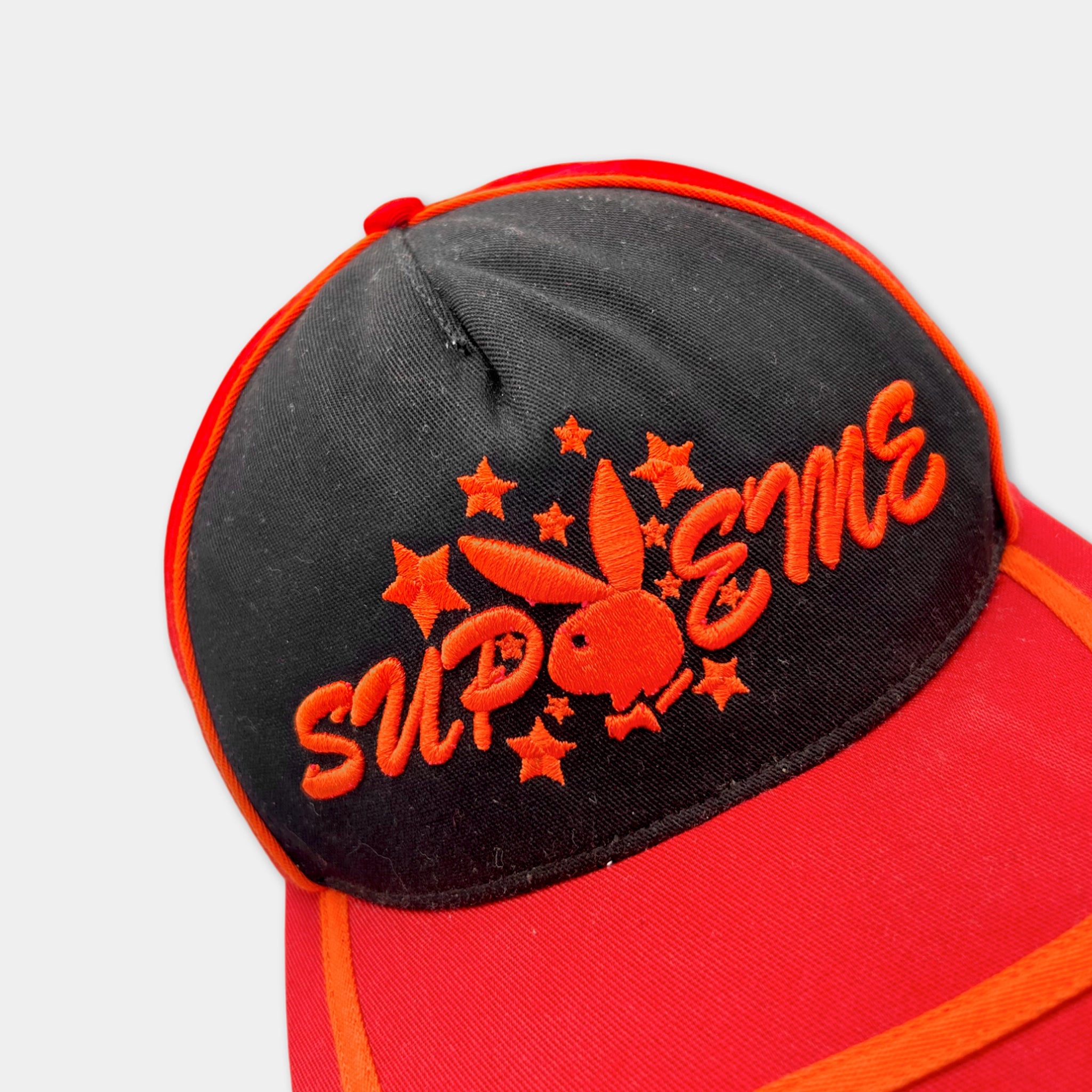 A red baseball cap with a black brim and a black and orange embroidered logo on the front.